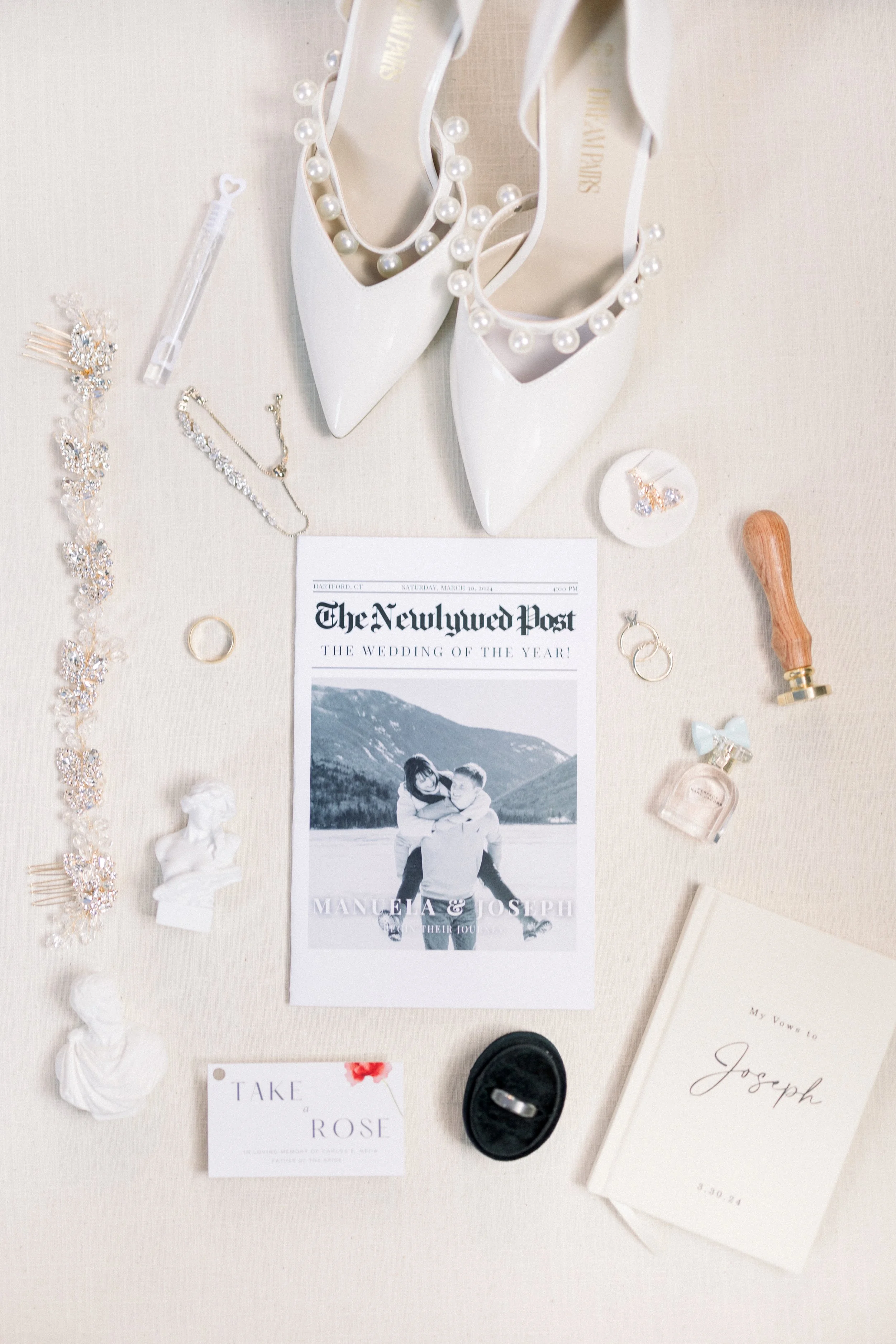 Wedding accessories and decor including white high heels with pearls, jewelry, a wedding ring, perfume, a marriage certificate, and a printed wedding invitation featuring a photo of a couple and the text 'The Newlywed Post'.