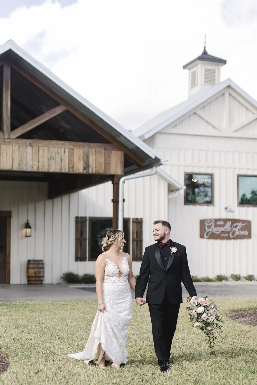 Bride and groom walk together in front of the white barn at Granville Farms in Lake Helen, Florida