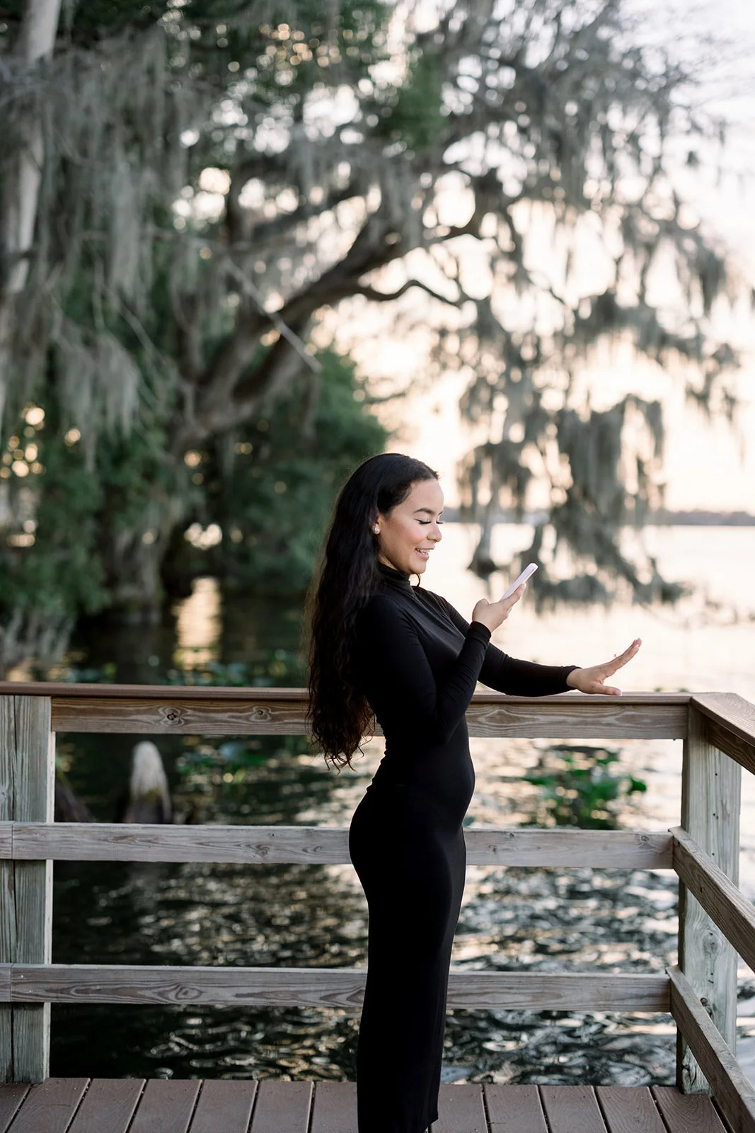 Smiling woman on a lakeside dock beneath Spanish moss-draped trees at golden hour in Central Florida