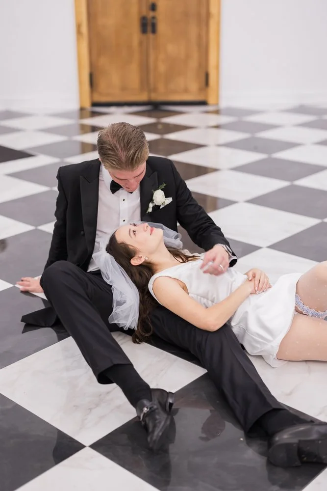 Bride and groom lying on a black and white checkered floor at Whitewood Ranch, photographed by Created by Patty