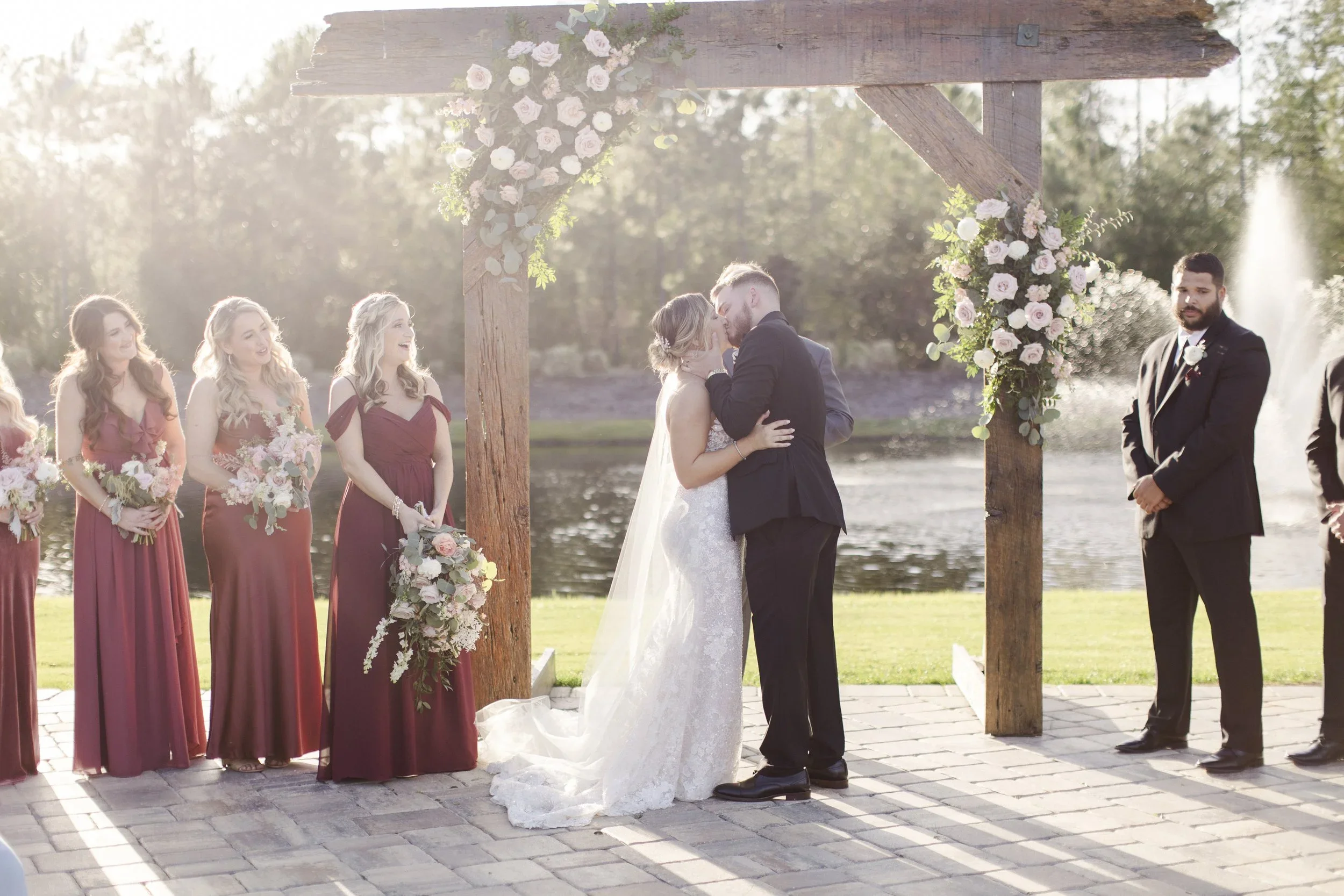 Bride and groom kiss under a wooden arbor during their outdoor ceremony at Granville Farms in Lake Helen, Florida