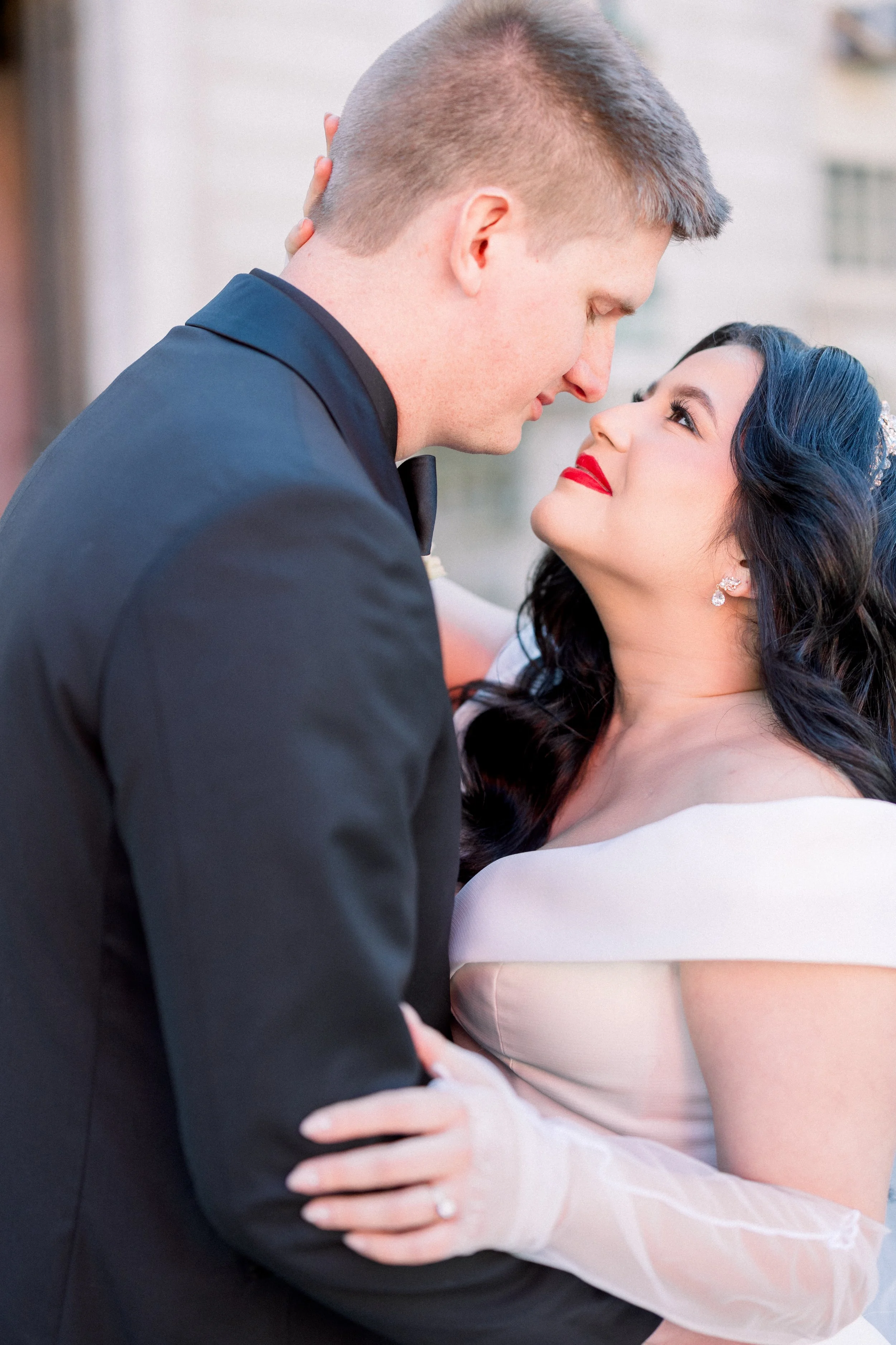 Close-up of a bride and groom during their wedding, looking into each other's eyes, with the groom holding the bride as she smiles and gazes upward, outdoors.