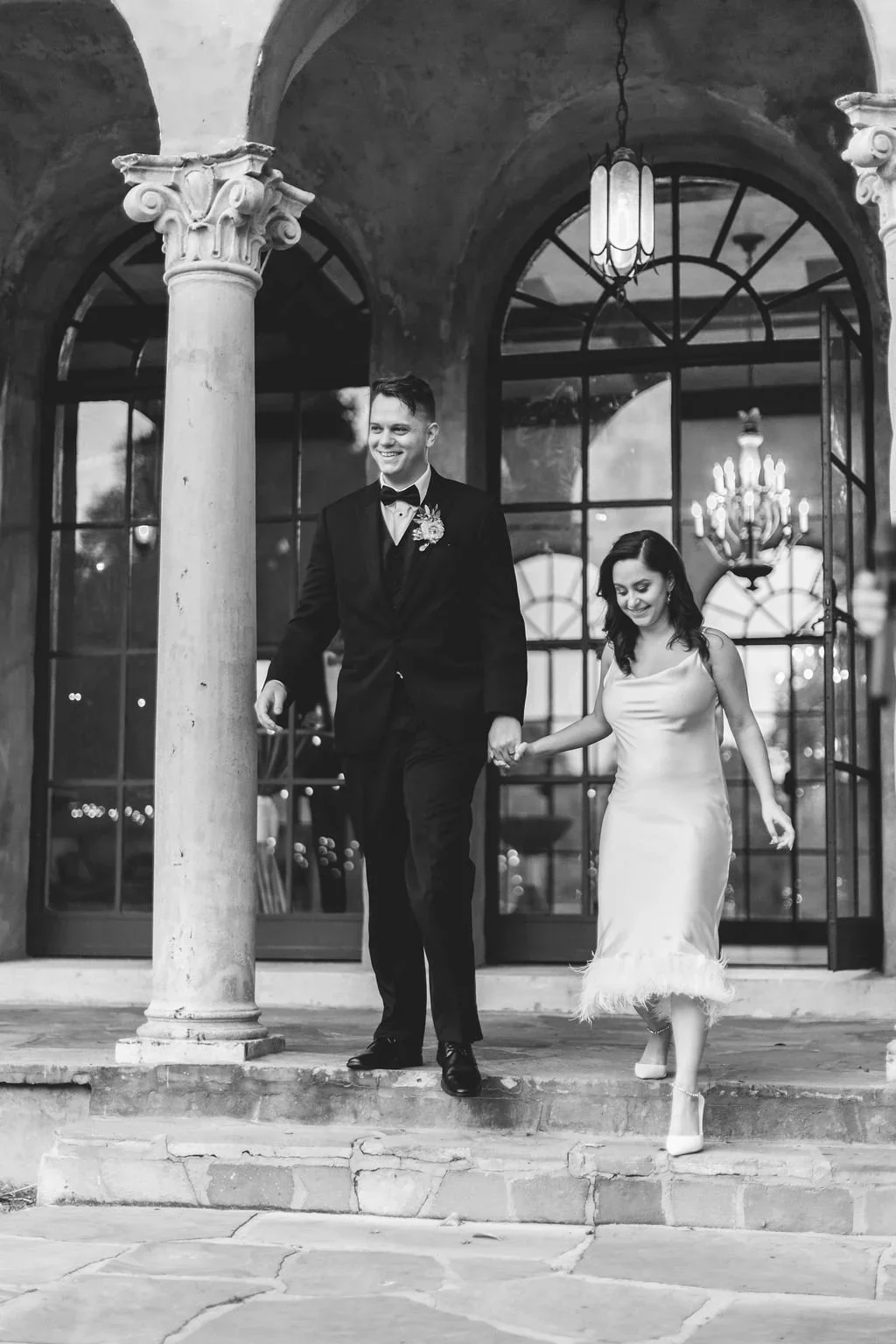 Black and white photo of the bride and groom walking out of a stone archway at the Howey Mansion