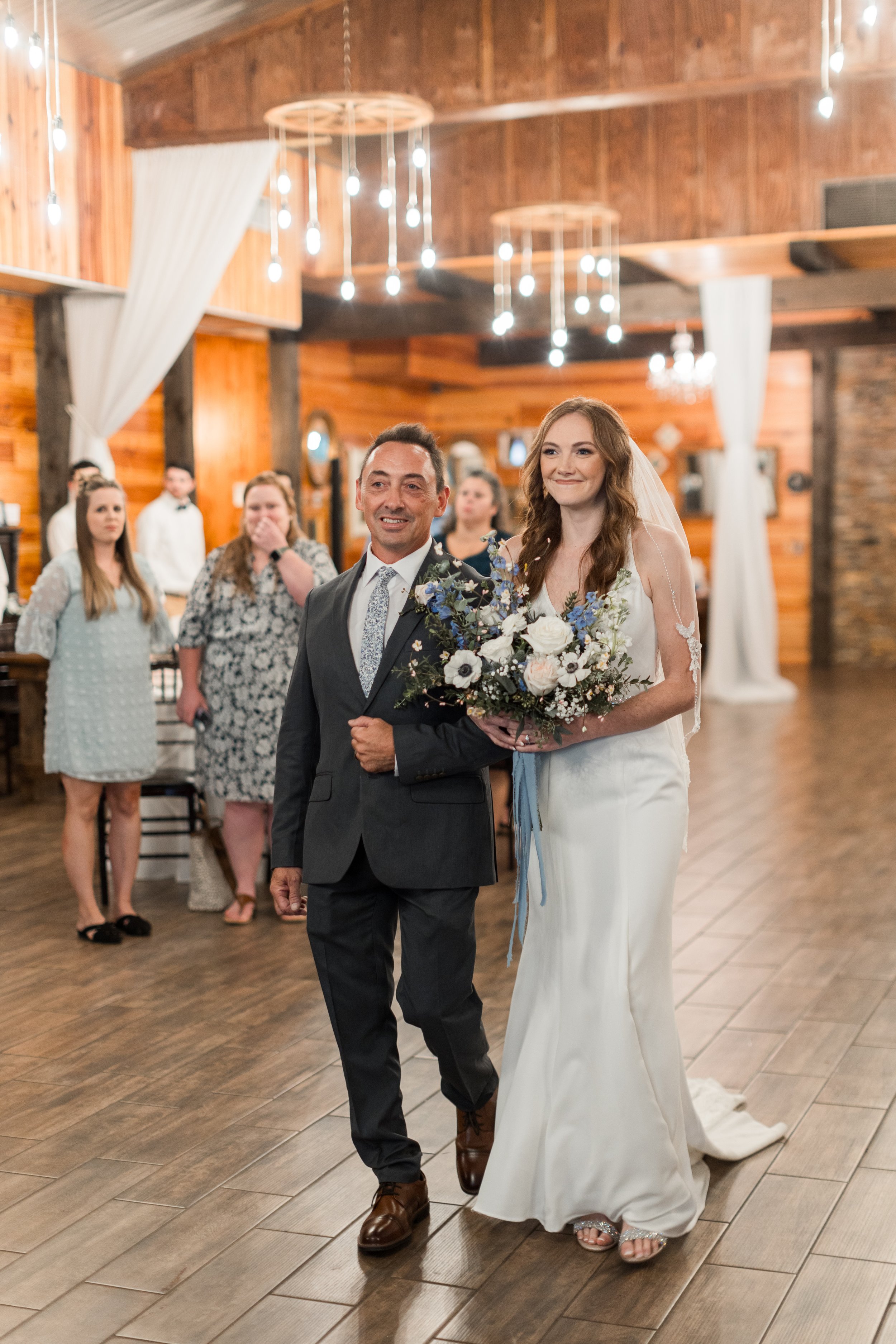 Bride walks down the aisle with her father under chandeliers inside Club Lake Venue