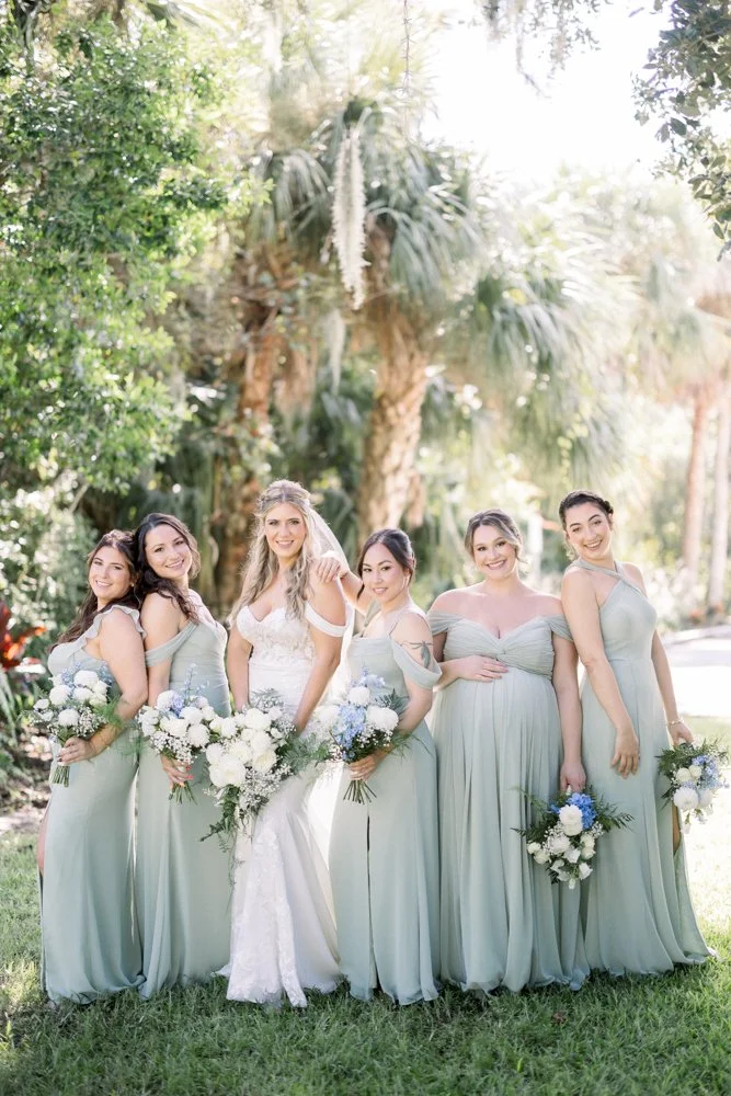 Bride with her bridesmaids in sage green dresses under palm trees at The Grand 721 wedding venue