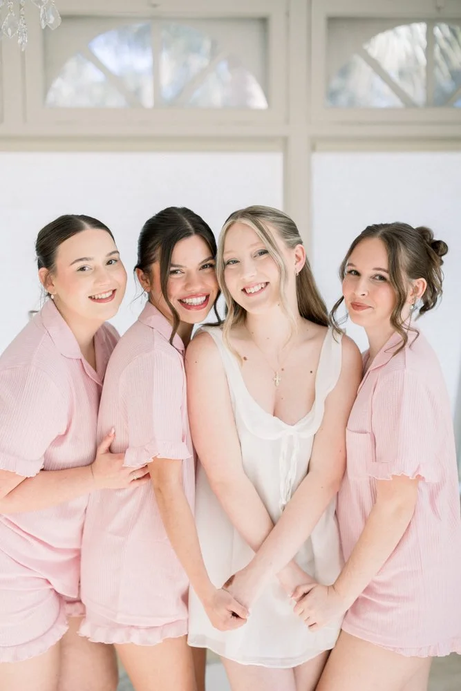 Bride laughing with her bridesmaids in pink robes while getting ready at Lakeview Gardens