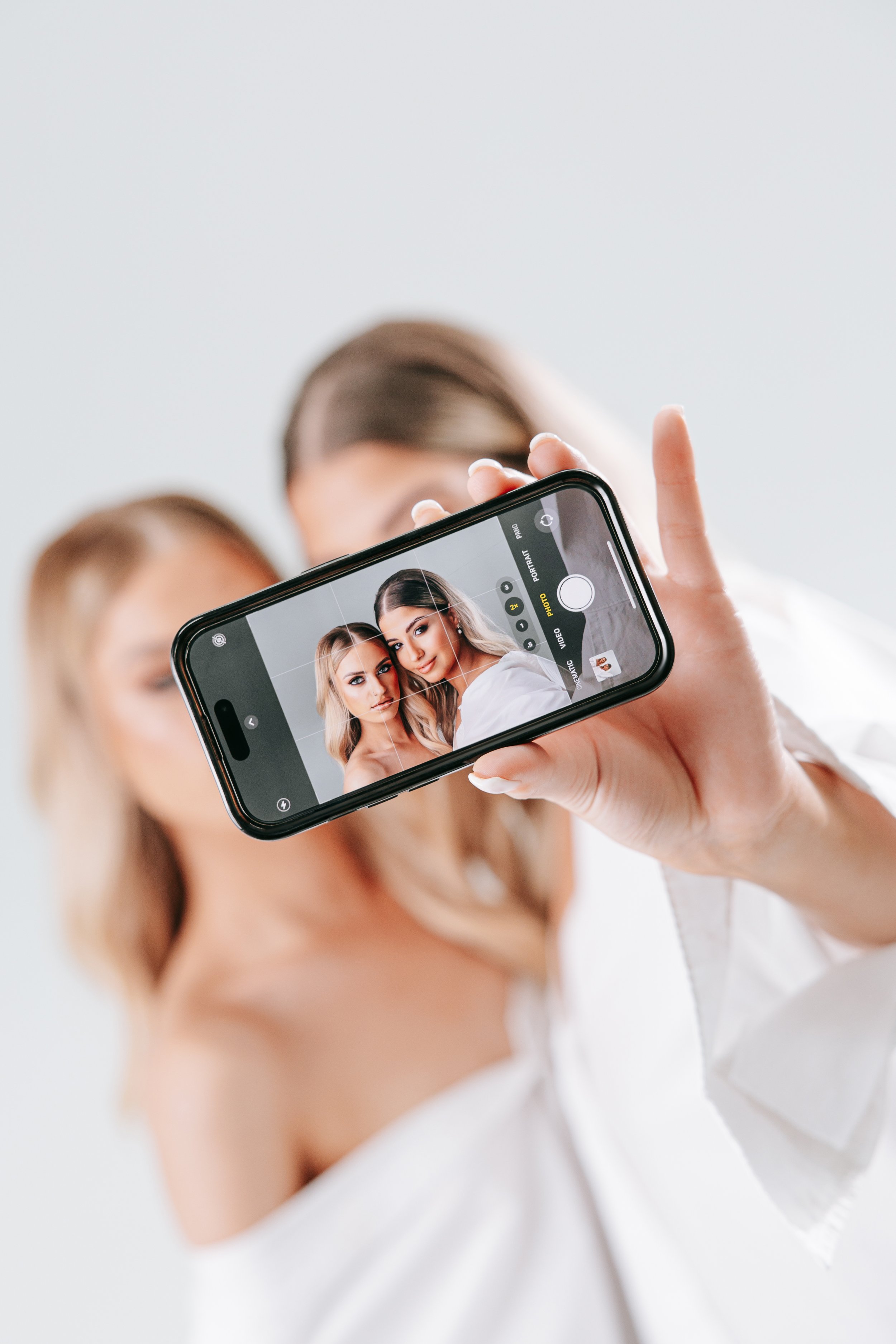 Person taking a selfie using a smartphone, with the phone screen showing two women with blonde hair posing for the photo.