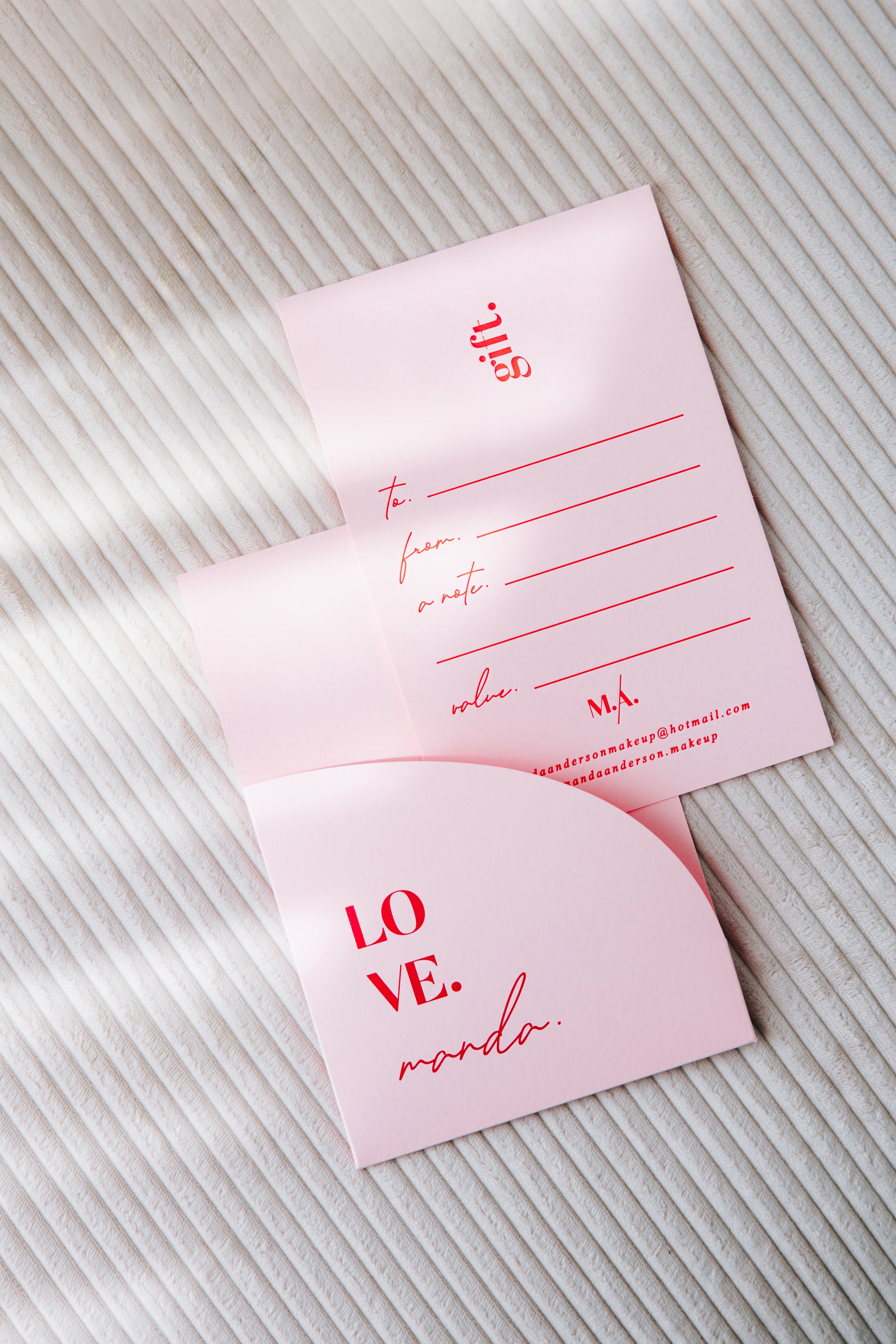 Pink love letter with red text, featuring lines for recipient and sender, and email addresses at the bottom, placed on a textured, off-white fabric surface.