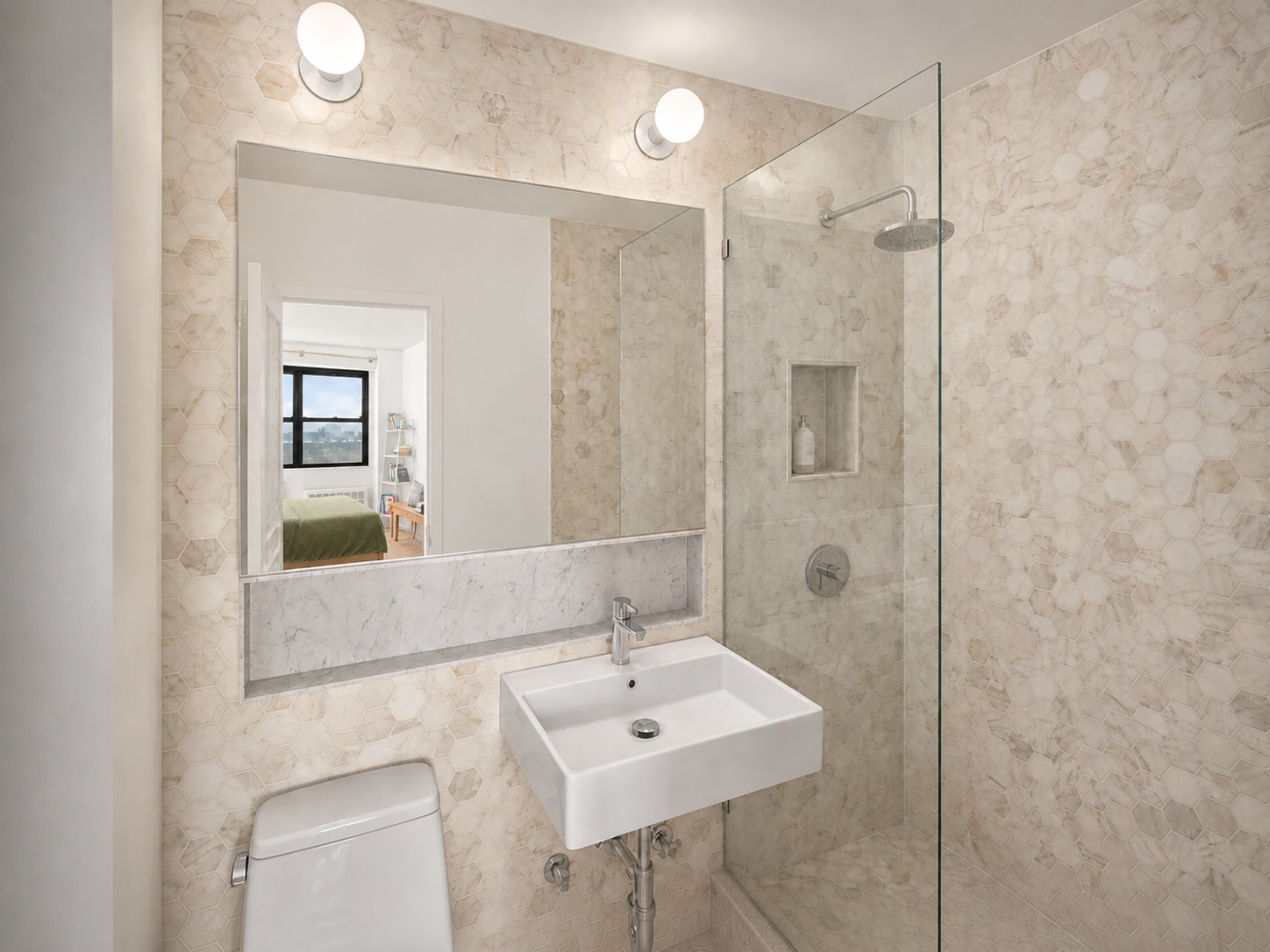 Small modern bathroom with beige hexagonal tile walls and floor, a white wall-mounted sink, a toilet, and a walk-in shower with a glass partition and built-in niche for toiletries. A large mirror above the sink reflects a bedroom with a bed, bookshelf, and window.