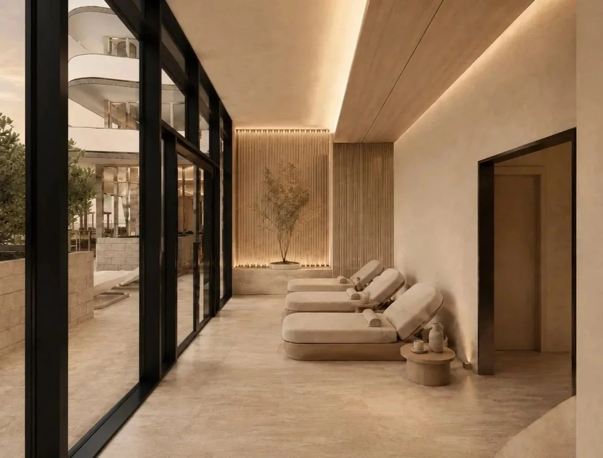 Modern indoor space with a row of lounge chairs, small side table, potted plant, and large glass sliding doors leading outside, illuminated with warm lighting.