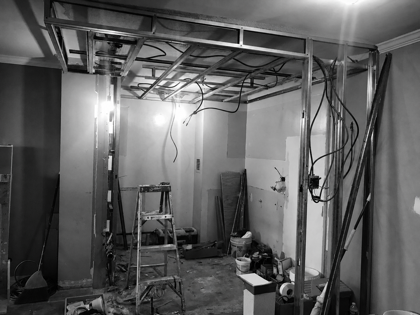 This image shows a room under renovation with exposed metal framing, construction tools, ladders, and wiring.