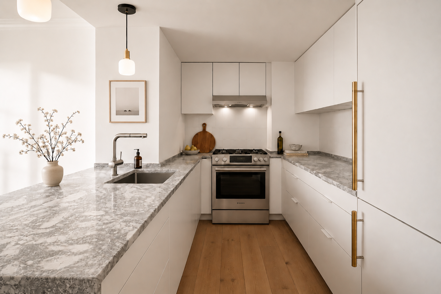 Modern kitchen with white cabinets, gray marble countertops, stainless steel oven, and minimal decor including a vase with flowers, a framed photo, and a cutting board.