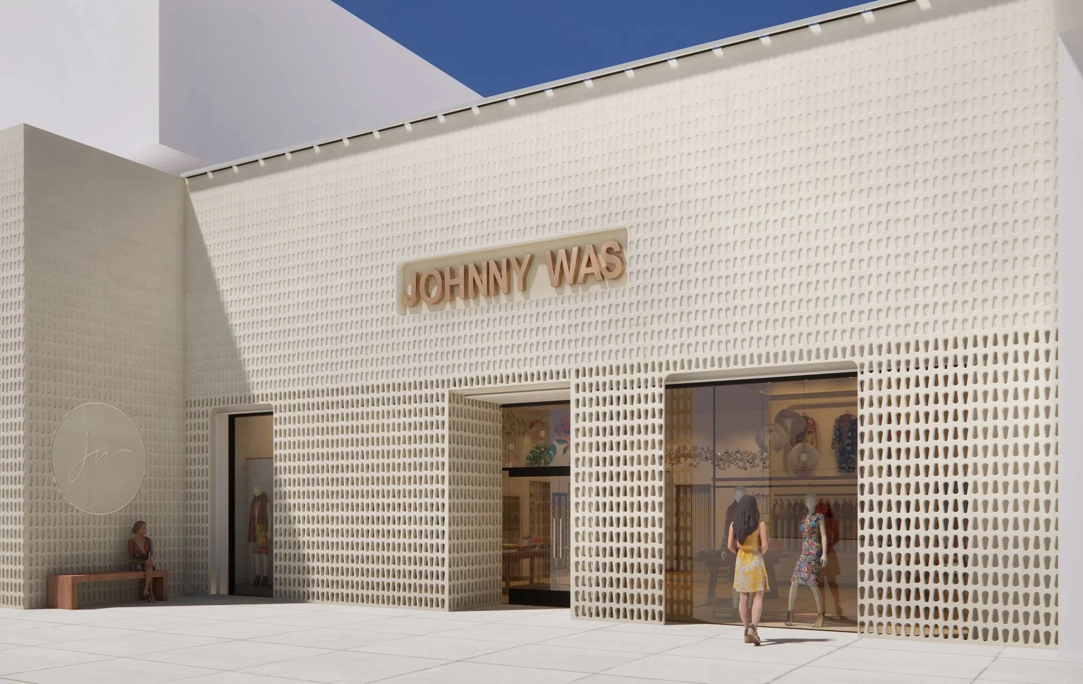 A modern storefront with a textured cream-colored facade featuring rectangular cutouts. The sign above the entrance reads 'JOHNNY WAS.' Large glass windows display clothing and mannequins inside. There are three women walking past the store, one woman sitting on a bench, and a man visible inside the store through the windows.