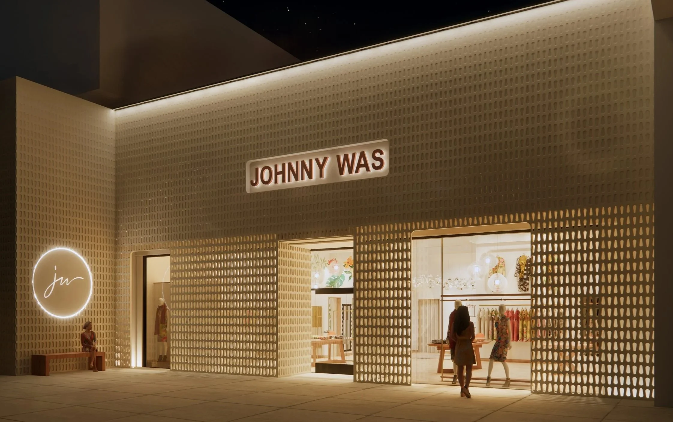 Exterior view of a retail store with distinctive beige perforated walls, illuminated sign with red letters reading 'JOHNNY WAS', mannequins displaying clothing inside, and a woman walking past.