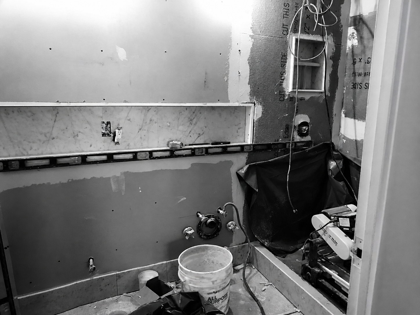 A bathroom under renovation with exposed plumbing and unfinished walls, construction materials, and tools scattered around.