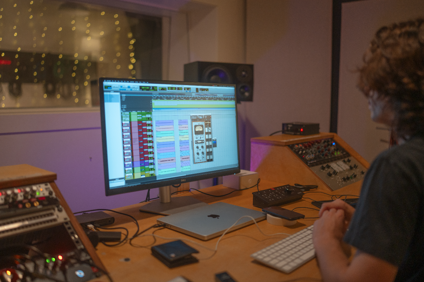 A person working on music production in a recording studio, with a computer screen displaying a digital audio workstation and various audio equipment around.