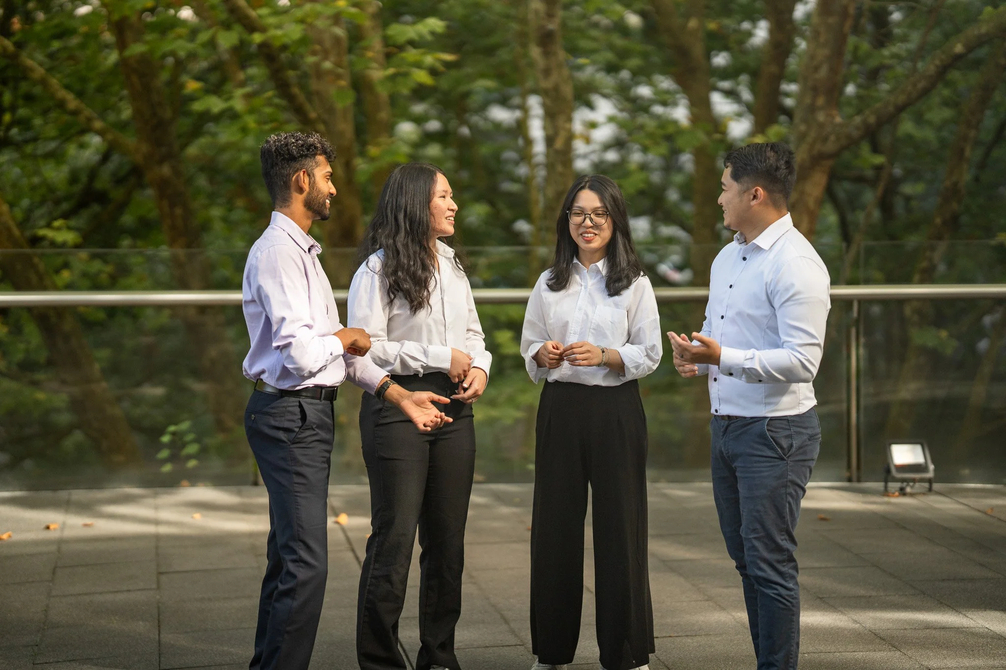 Four diverse young professionals in business attire having a conversation outdoors.