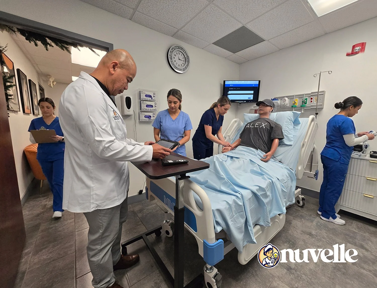 A group of medical professionals and a patient in a hospital room. The patient is lying on a hospital bed, holding hands with a nurse. A doctor in a white coat is using a tablet. Other medical staff are working or taking notes nearby.