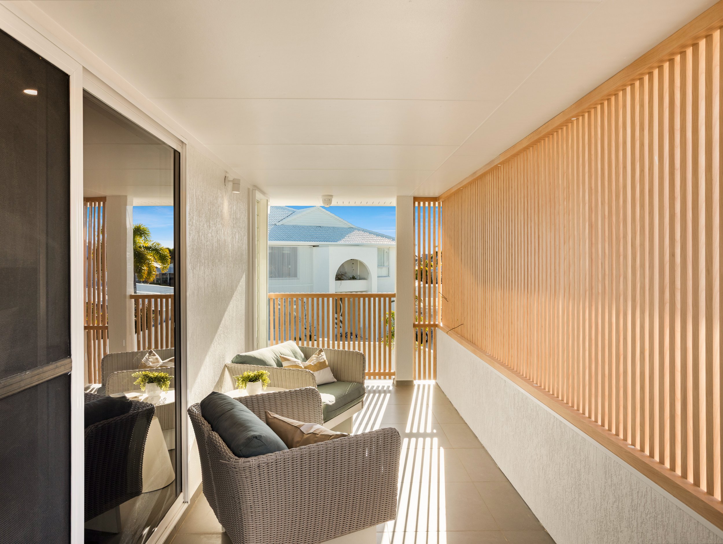 A sunlight balcony with wooden slats and modern furniture overlooking canals of Redcliffe, Brisbane.