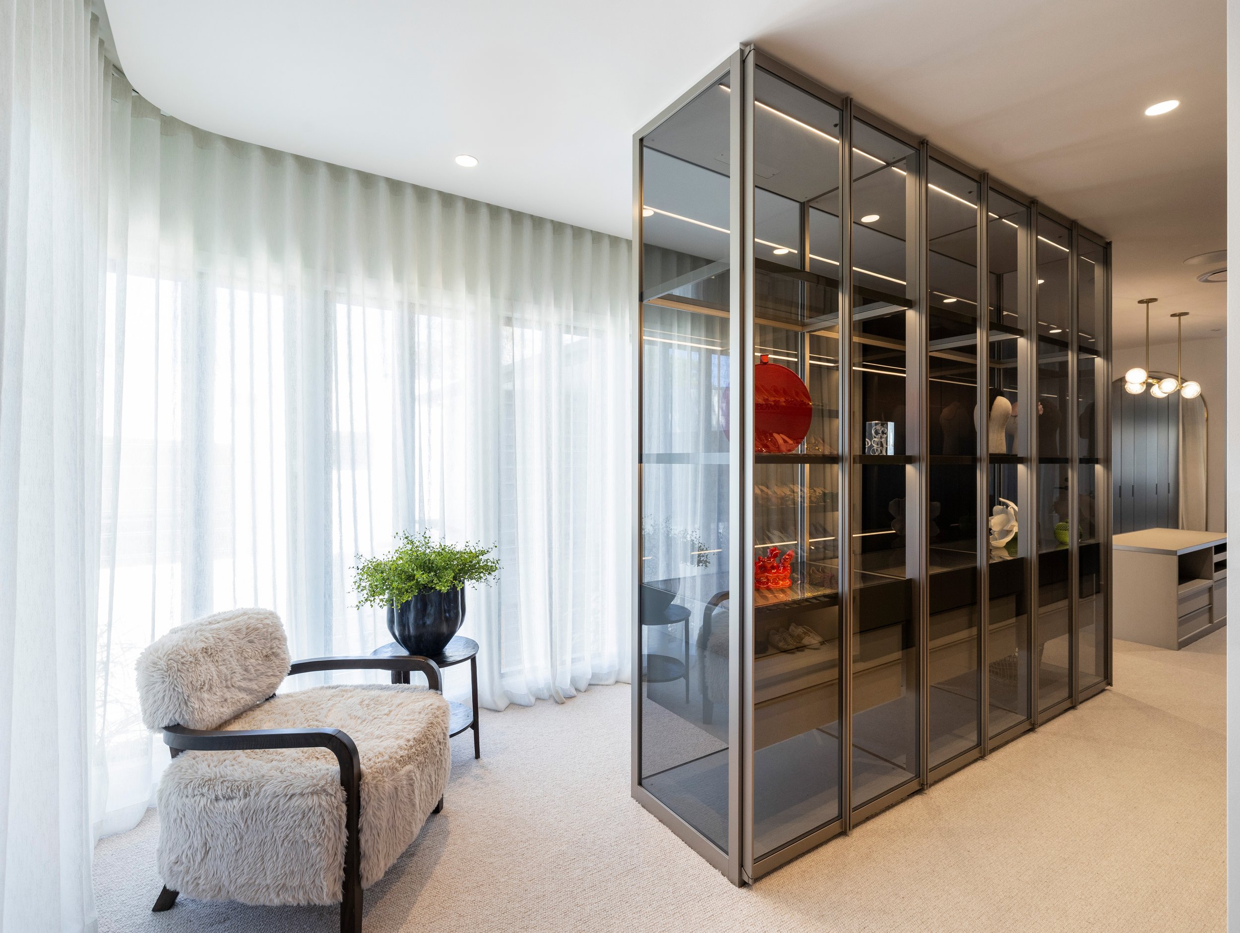 Luxury in-built walk in wardrobe with a unique large glass shelving and a luxury chair and a large window overlooking Brisbane City.
