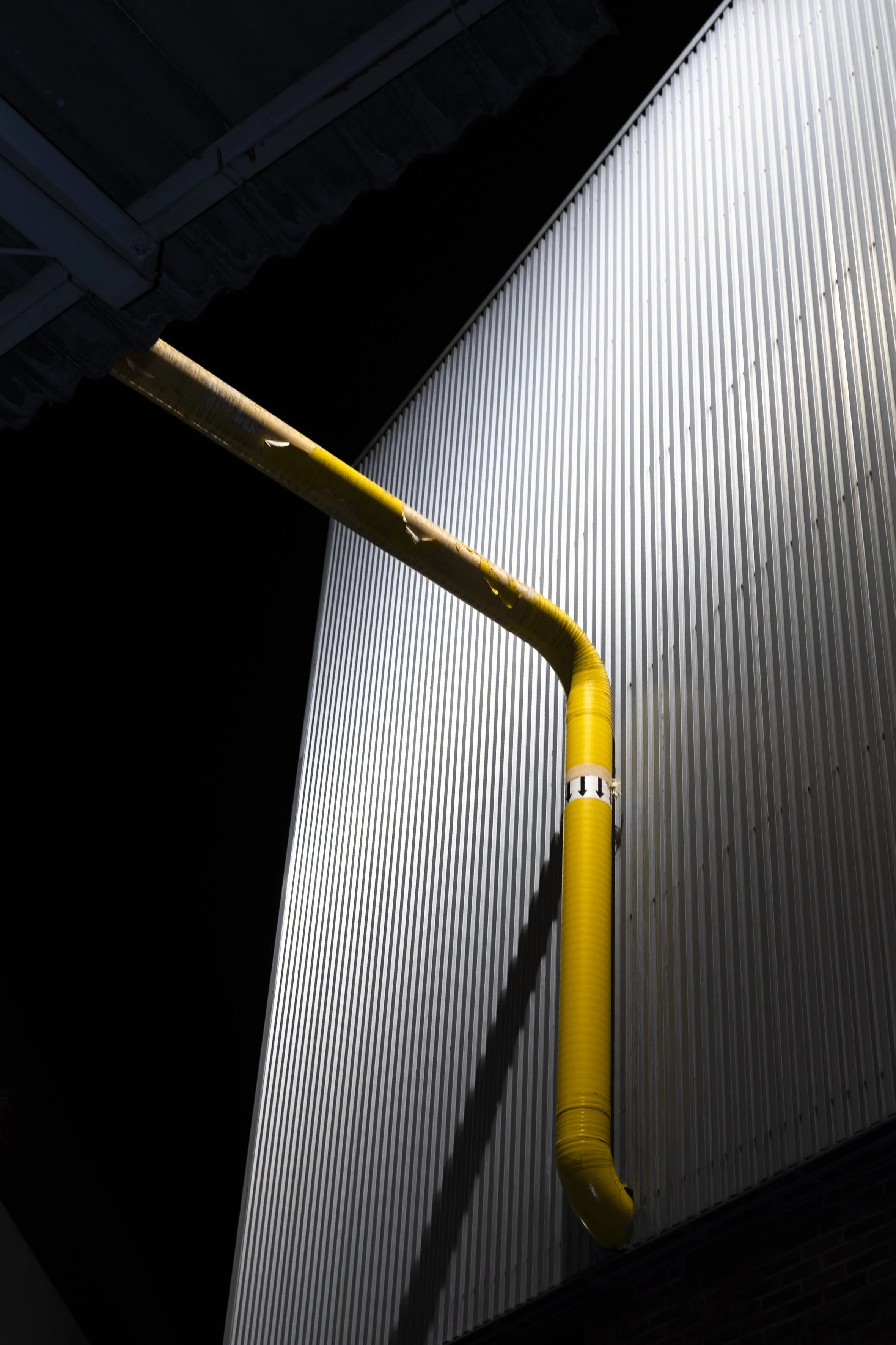 Gelber Rohr an einer silbernen Wand in einer Industriehalle.