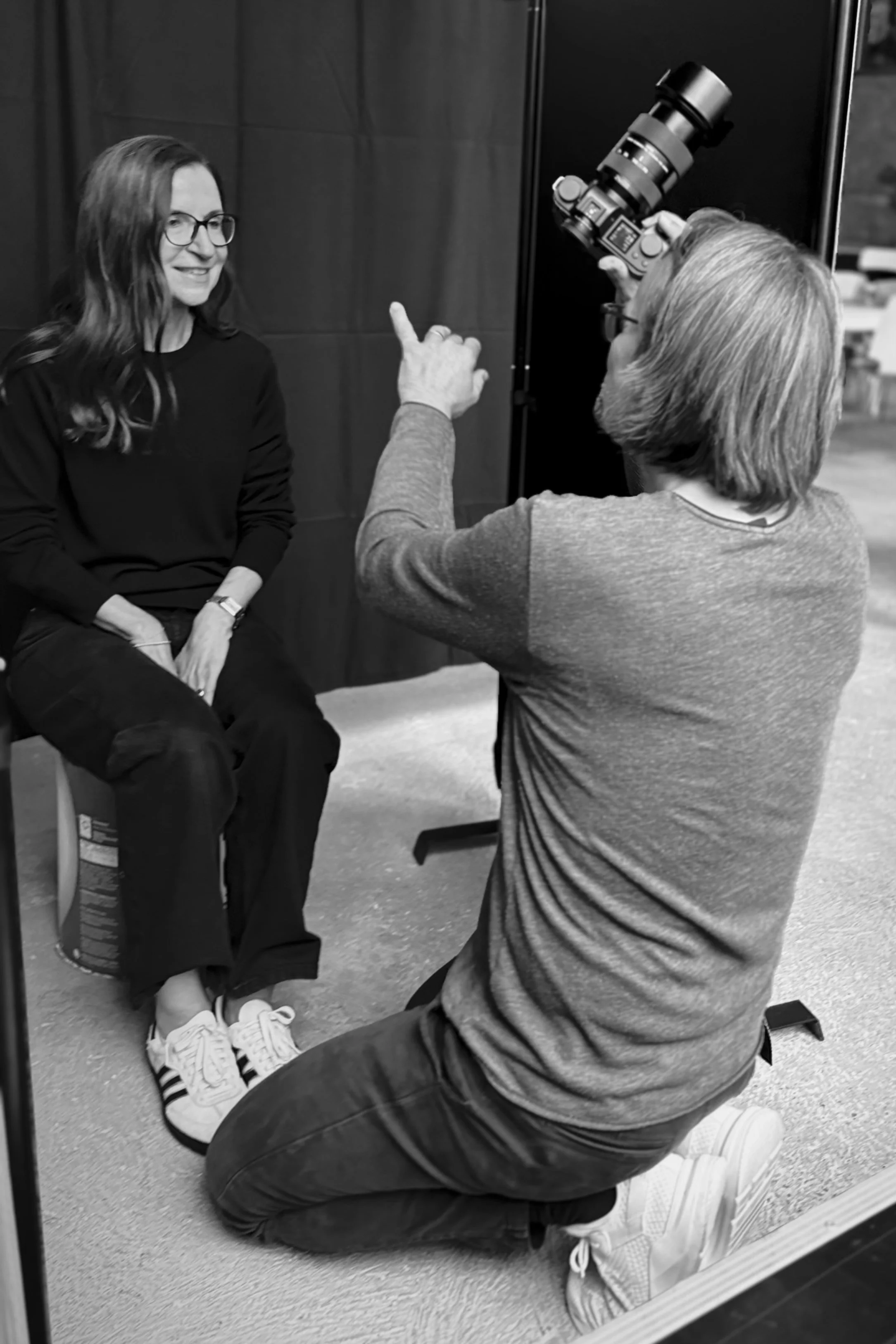 Frau sitzt auf einem Stuhl, während ein Fotograf sie für ein Portraitfoto aufnimmt