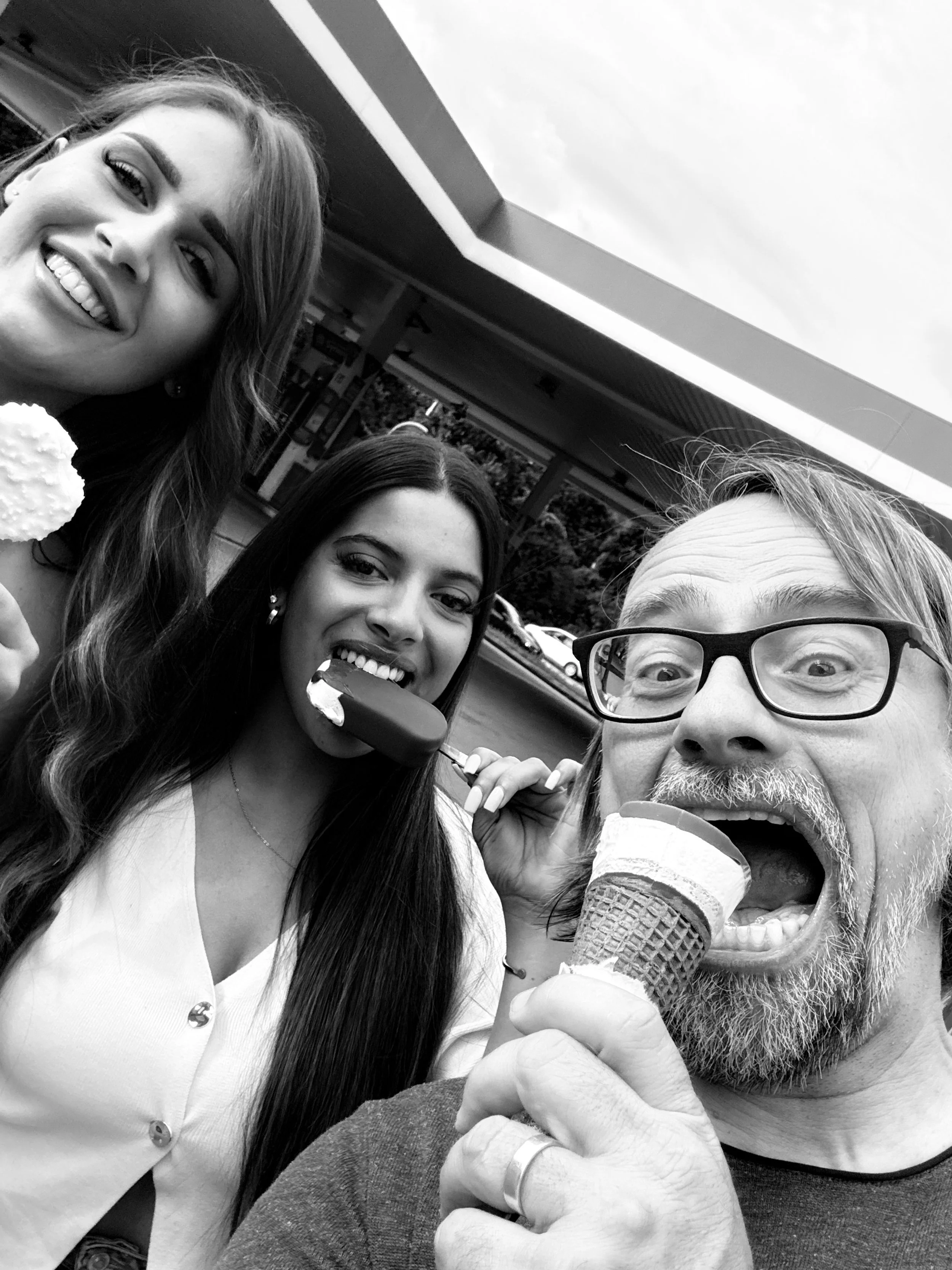 Drei Menschen, zwei Frauen und ein Mann, lachen und essen Eis vor einem Automat bei Sonnenwetter. Sie genießen ihren Tag gemeinsam.