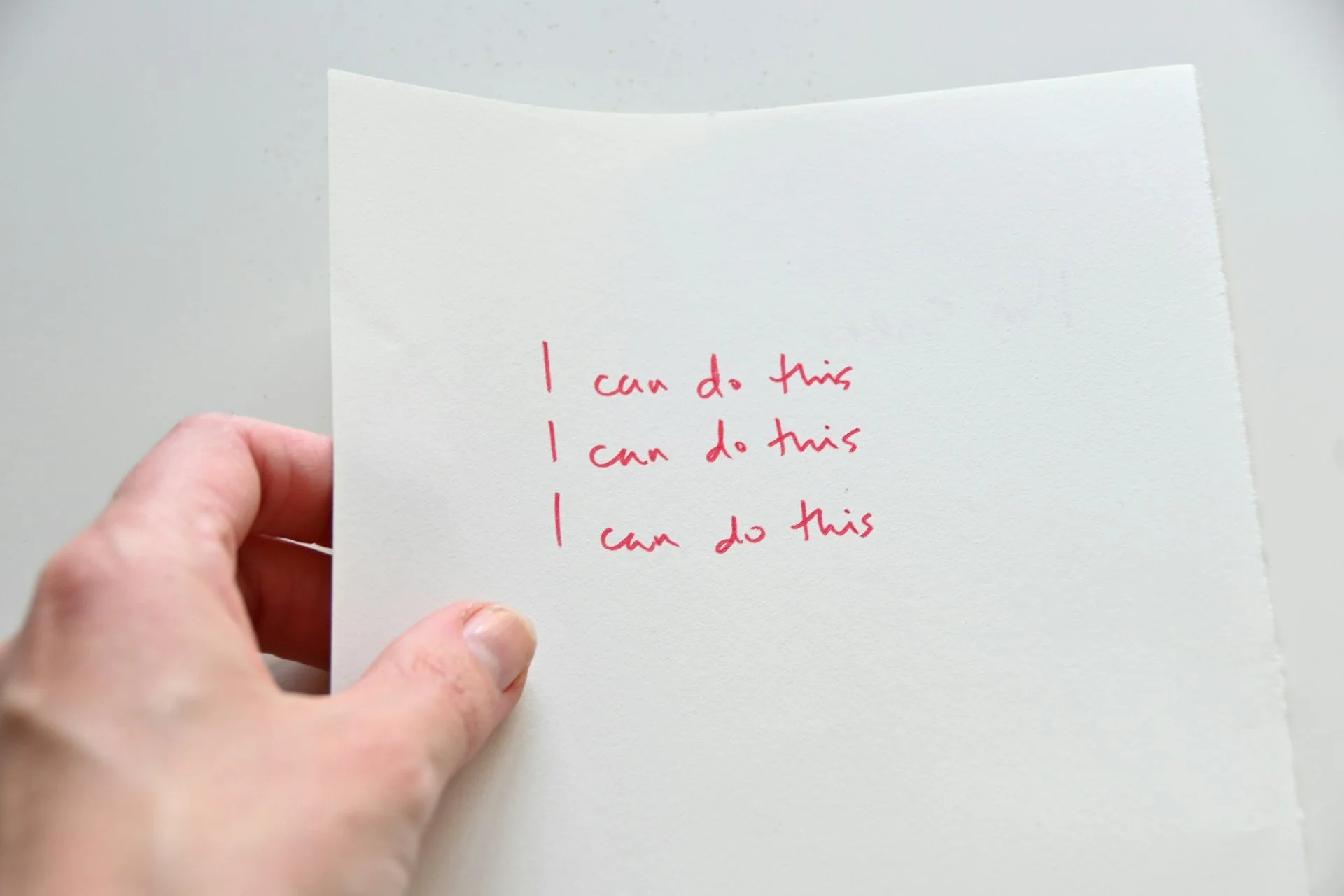a hand holding a  white piece of paper that says ''I can do this'' three times