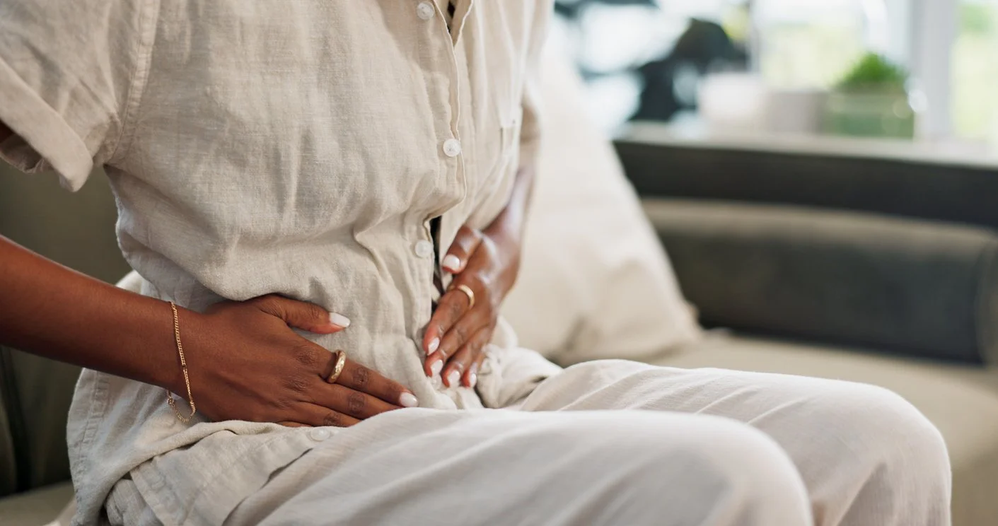 Person in a grey outfit gently placing hands on their belly for abdominal relief