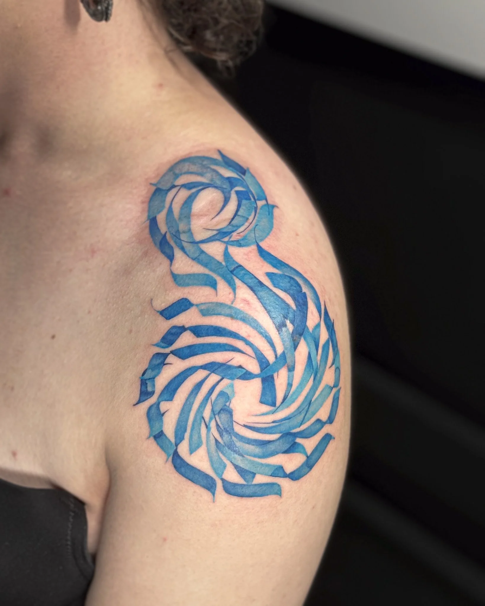 Close-up of a person's shoulder with a blue and gray rose tattoo.