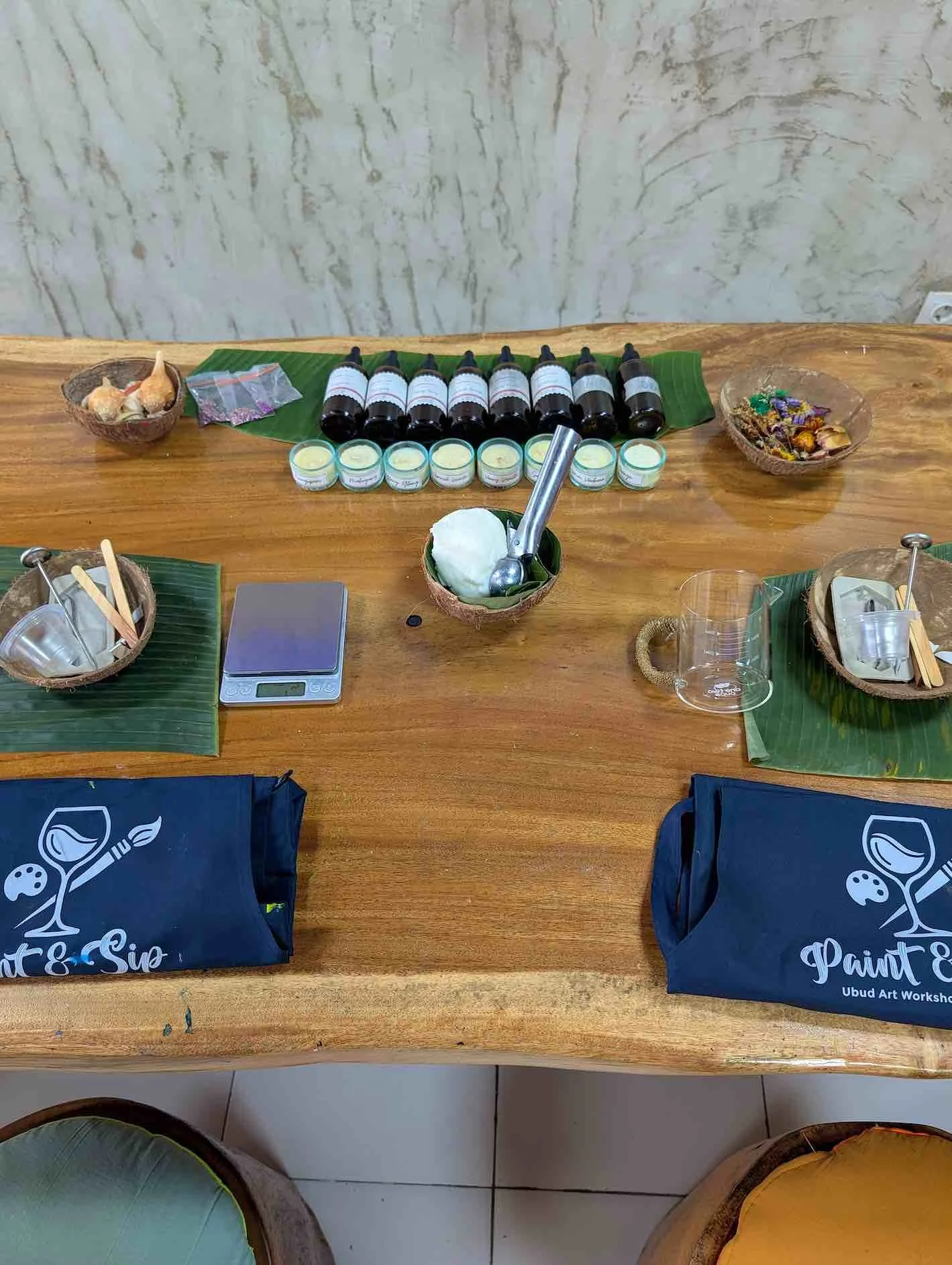 Table set with essential oils, small bowls, candles, leaves, and soap, likely for a wellness or spa workshop.