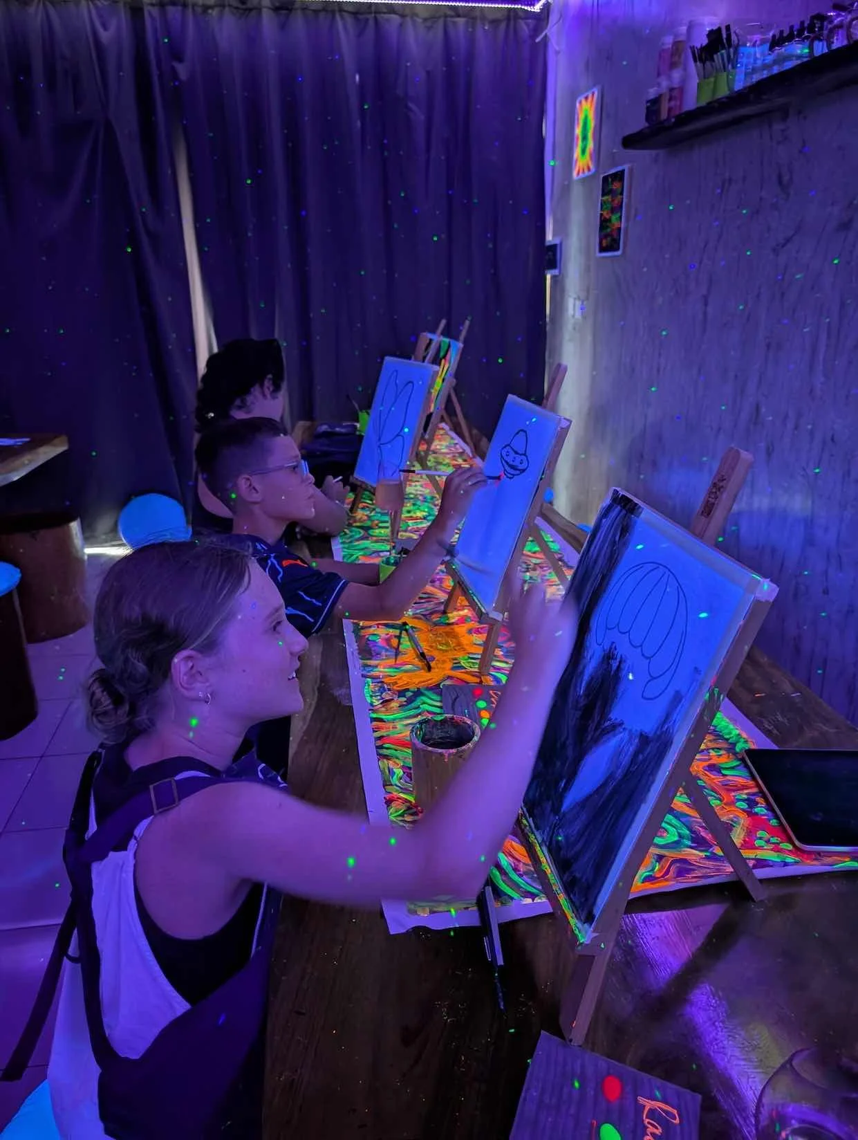 Children painting on canvases at a glow-in-the-dark art party with black light and neon decorations.