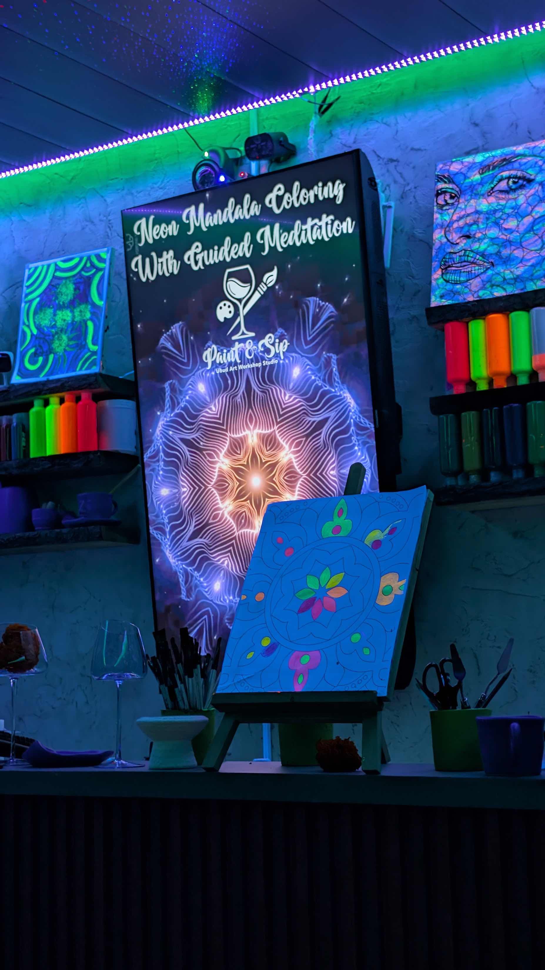 Neon sign promoting a neon mandala coloring activity with guided meditation at a paint and sip studio, with colorful artwork, supplies, and glowing decor.
