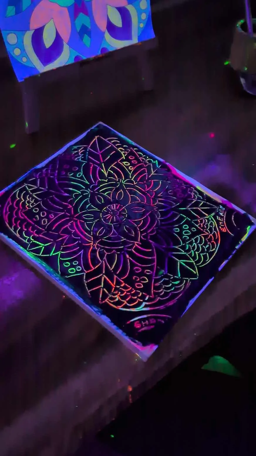 Black light poster with colorful floral and geometric patterns, illuminated by neon glow.