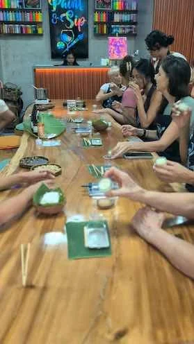 People gathered around a table celebrating a birthday with cupcakes and drinks in a decorated room.