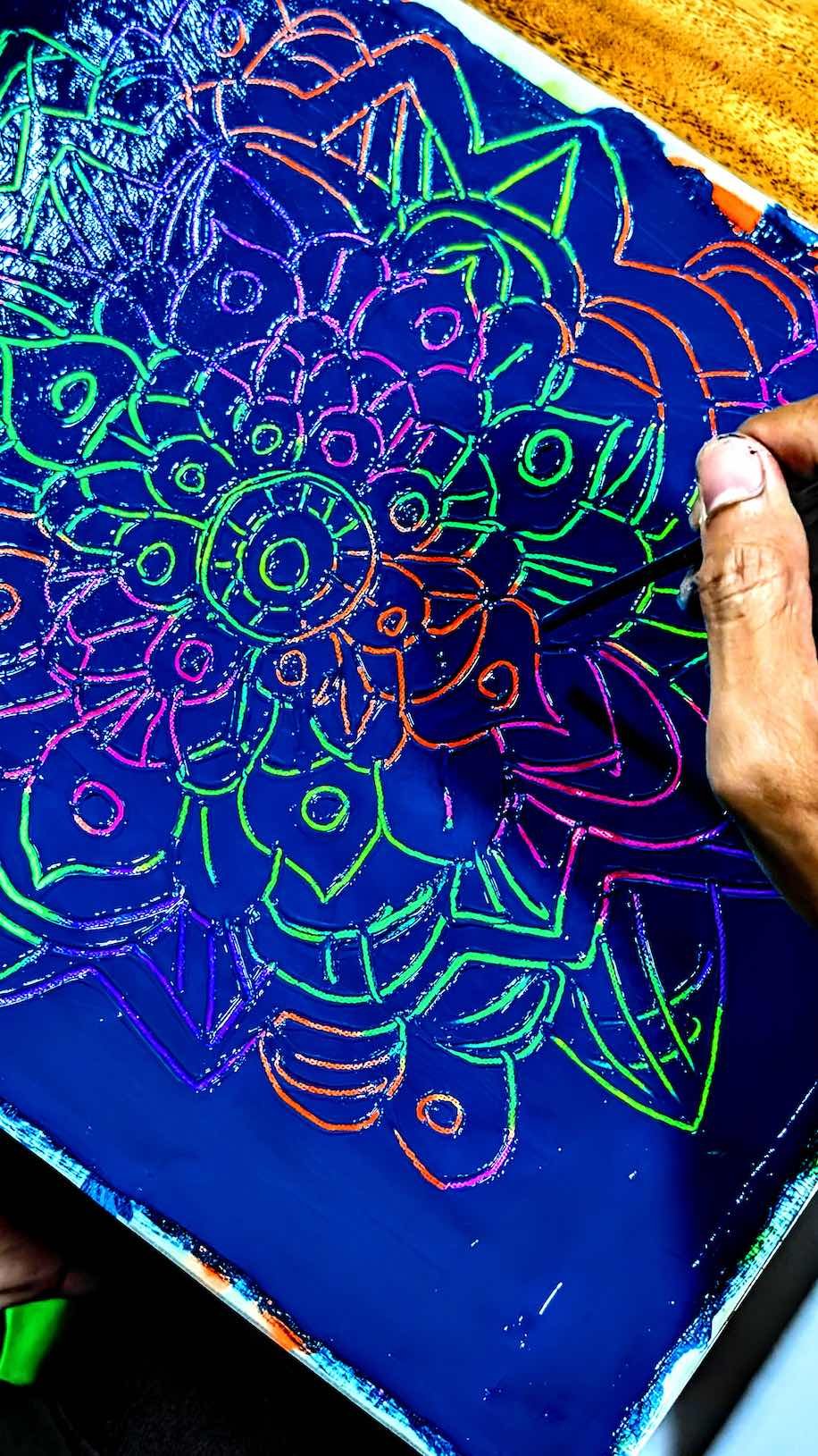 Hand drawing a colorful abstract floral design with neon-colored lines on a black surface.