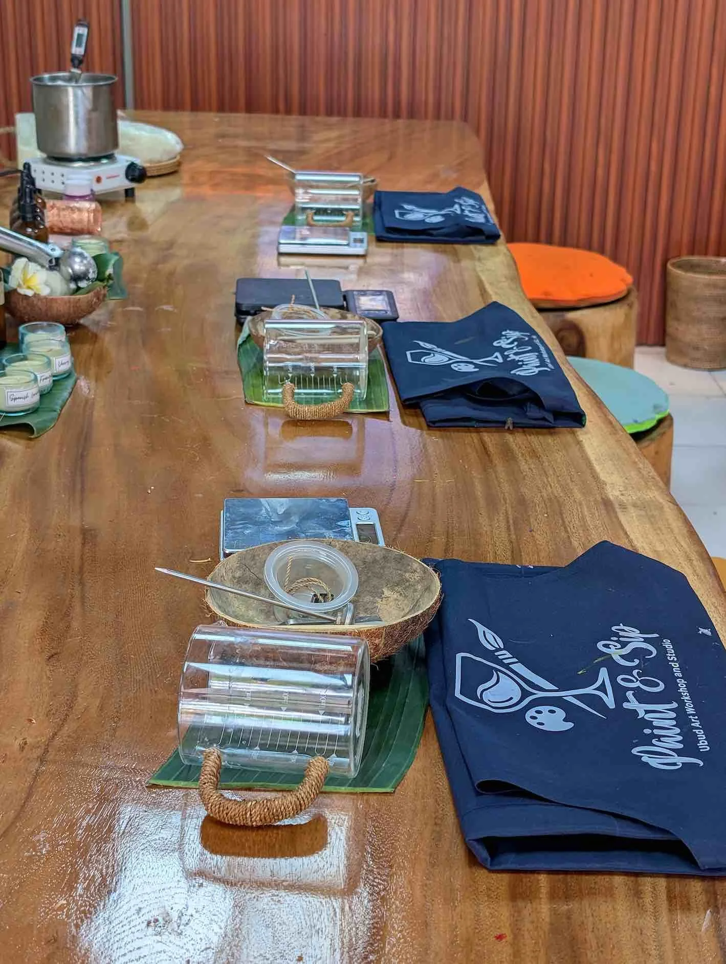 A wooden table set with black cloth napkins, glass containers with handles, a small bowl, a digital scale, and other small items in a cozy setting with wooden walls and colorful cushions in the background.