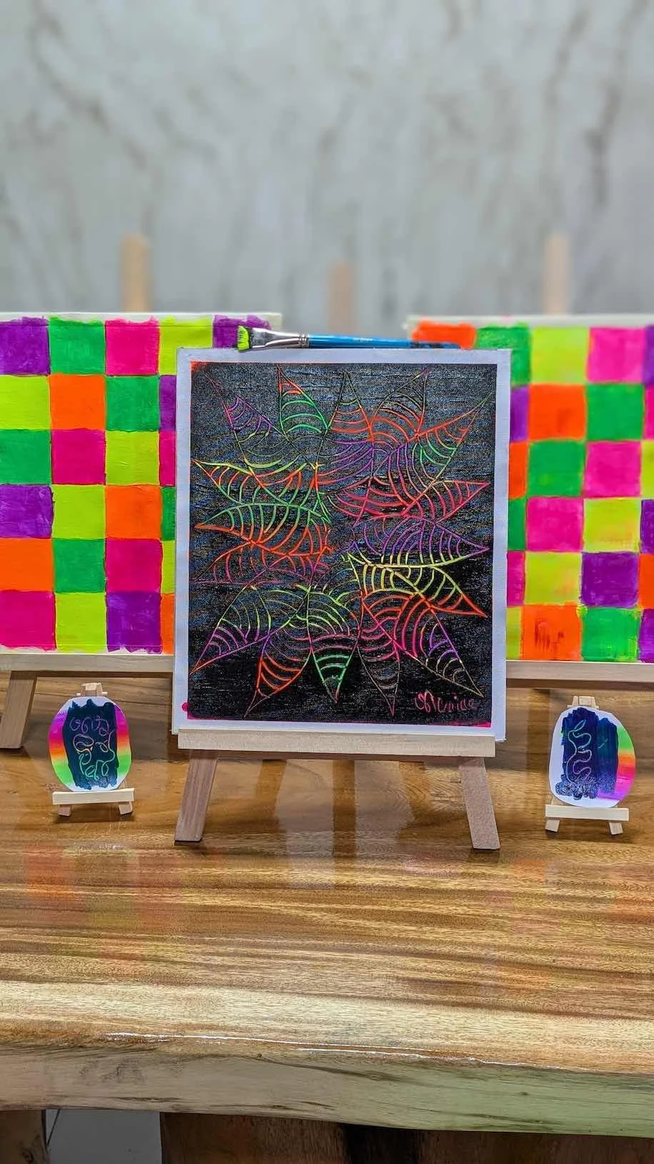 Neon-colored background with checkerboard pattern, a centrally placed black portrait with neon outlines of a person, and small artworks with neon rainbow backgrounds and intricate designs.