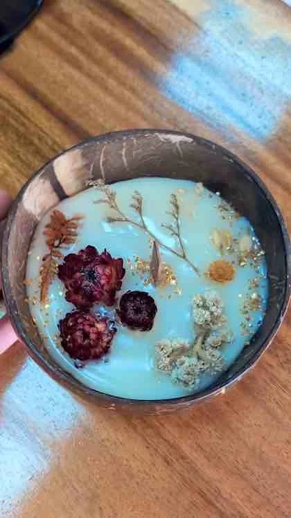 A candle in a glass holder decorated with dried flowers, berries, and leaves, placed on a wooden surface.