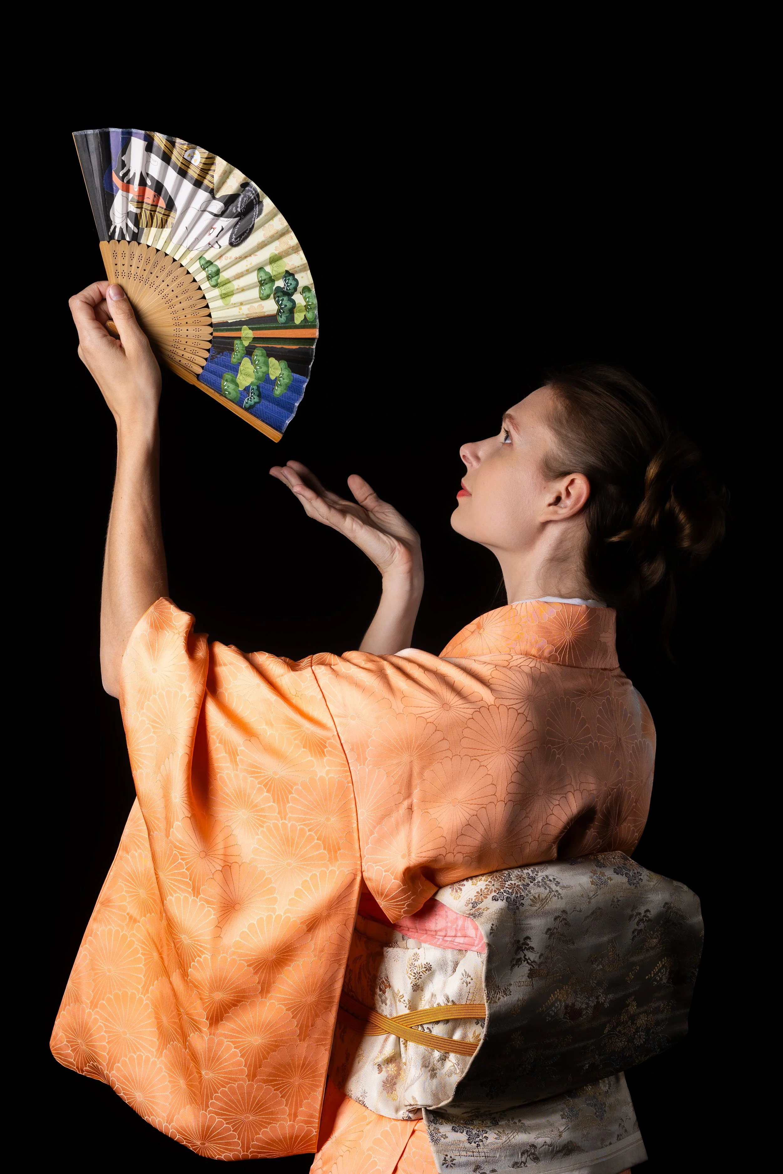 Une femme habillée d'un kimono traditionnel japonais orange avec un motif floral, tenant un éventail décoratif noir et blanc avec des motifs de souvenirs de japon