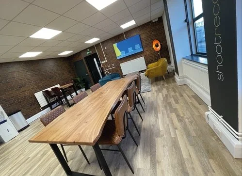 Interior of a modern office meeting room with a long wooden table, chairs, and lounge seating near large windows