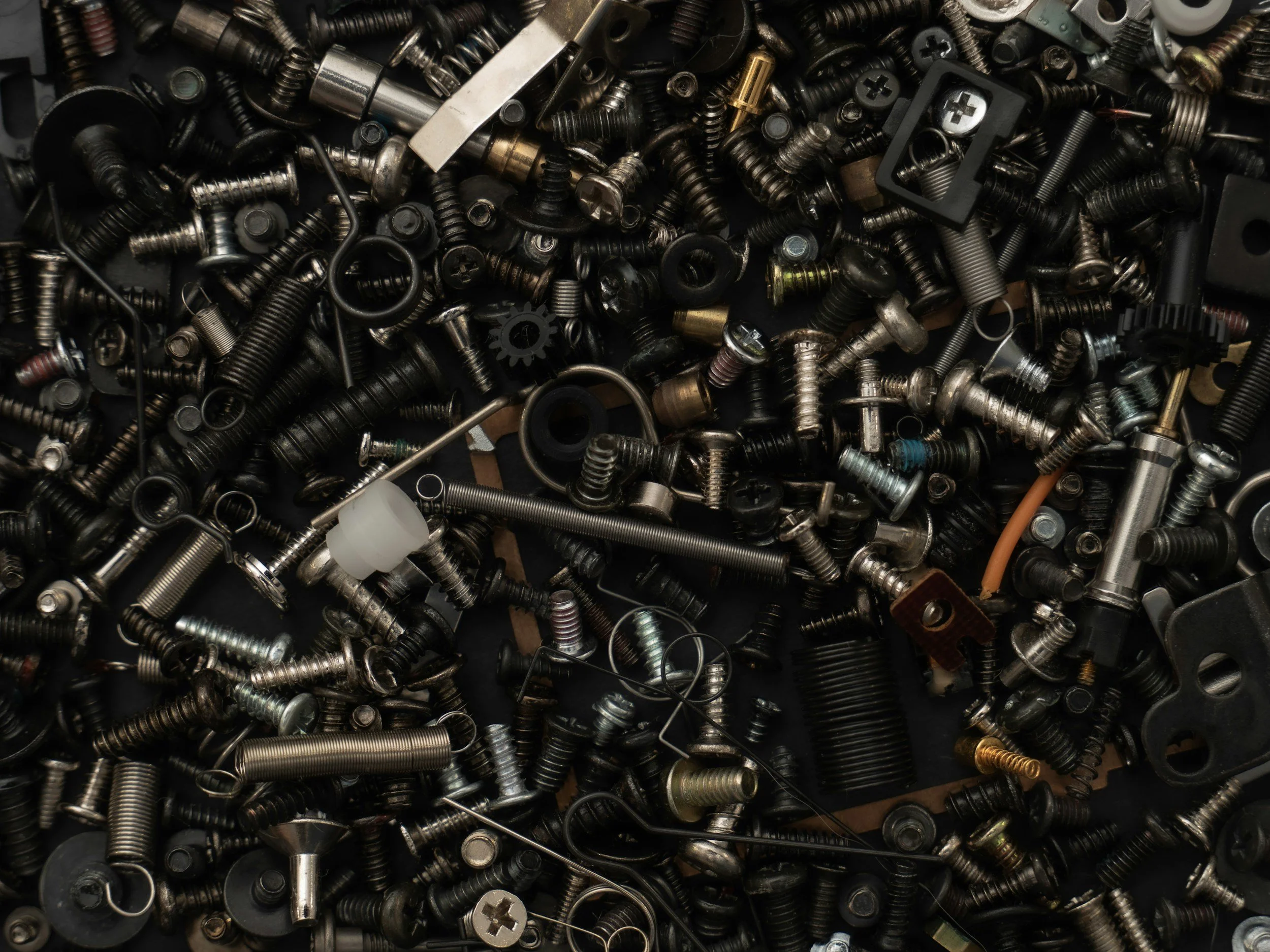 Billede af en stor bunke af forskellige skruer, bolte og metaldele i forskellige størrelser og former, spredt tilfældigt.