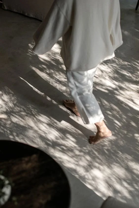Nahaufnahme einer Person, die barfuß auf einem Boden in einem Raum mit Licht- und Schattenmustern läuft, trägt weiße Kleidung.
