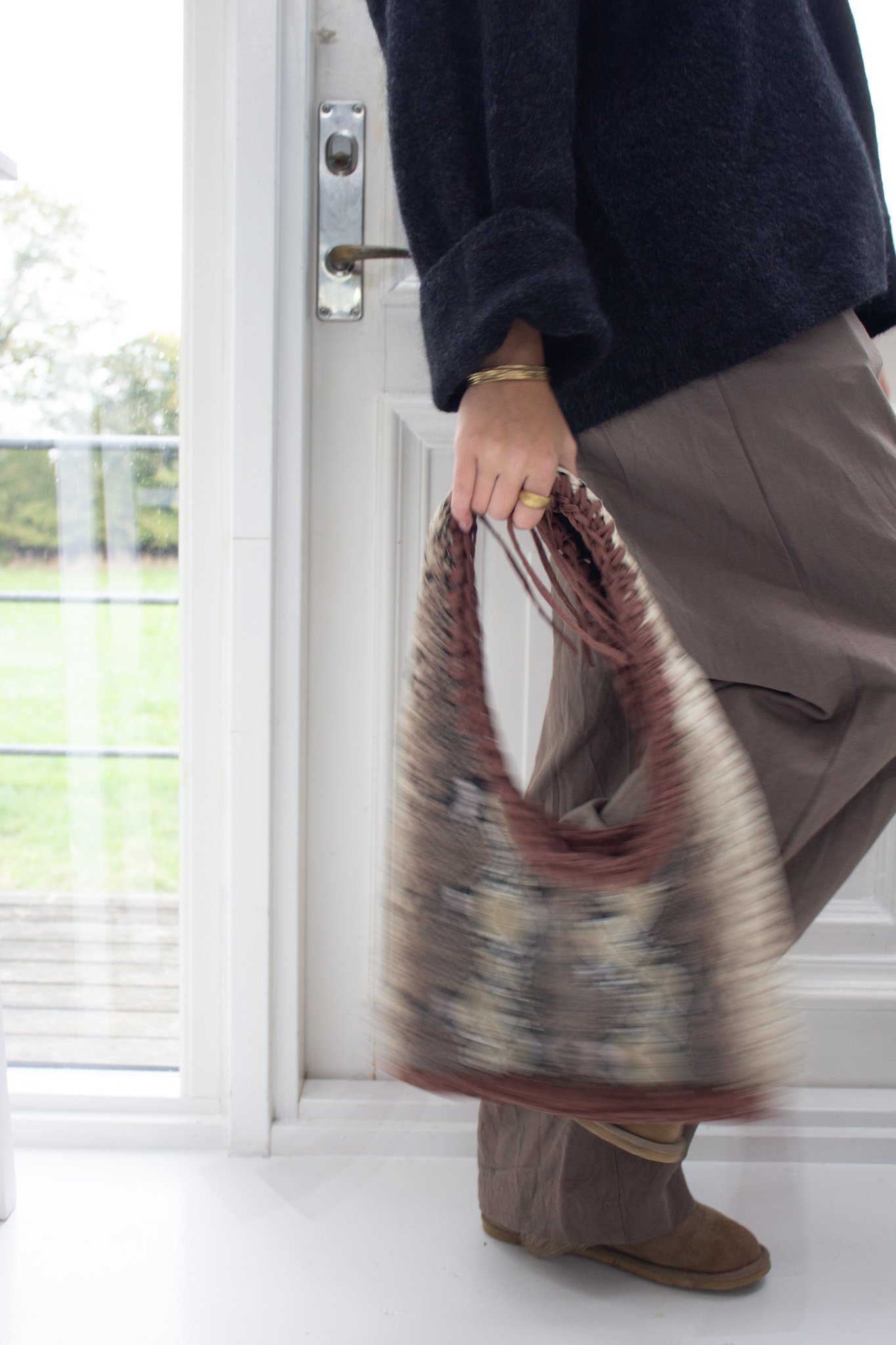 Person der skubber en dør åben med en taske i hånden, indendørs.