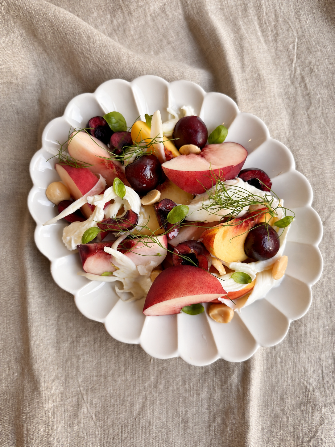 Overhead view of fresh white and yellow peach salad with black cherries, burrata, pickled fennel, basil and Marcona almonds.