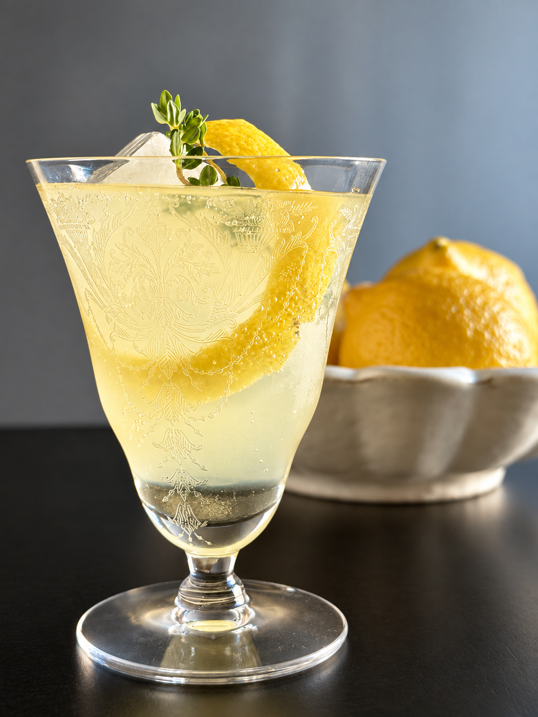Limoncello Spritz with lemon thyme and a wide lemon peel in an etched glass with bowl of lemons