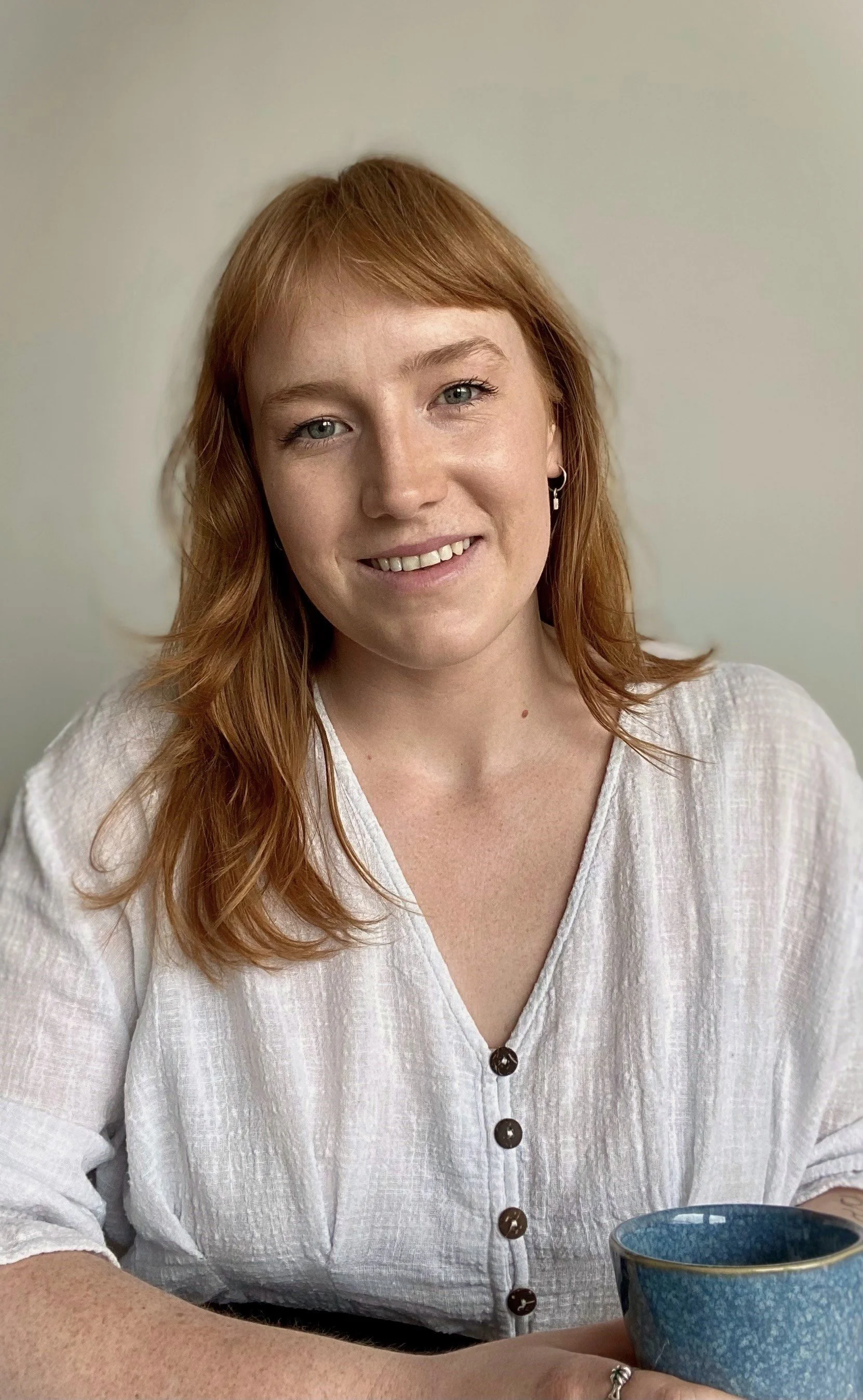 Portrait of a female Psychologist with red hair, wearing a white blouse, smiling, with a cup visible in the bottom right