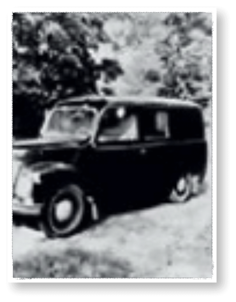 Historische Schwarzweißaufnahme eines alten Bestattungswagens der Firma Hasert, geparkt in ländlicher Umgebung mit Bäumen im Hintergrund; Teil der Firmengeschichte von Veerman Bestattungen Oranienbaum.