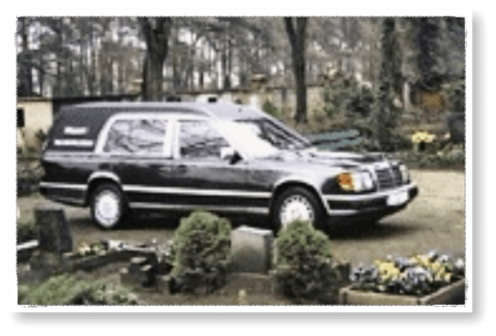 Farbaufnahme eines schwarzen Bestattungswagens der Firma Hasert auf einem Friedhof, umgeben von Grabsteinen, Blumen und Bäumen; dokumentiert die Firmengeschichte von Veerman Bestattungen Oranienbaum.