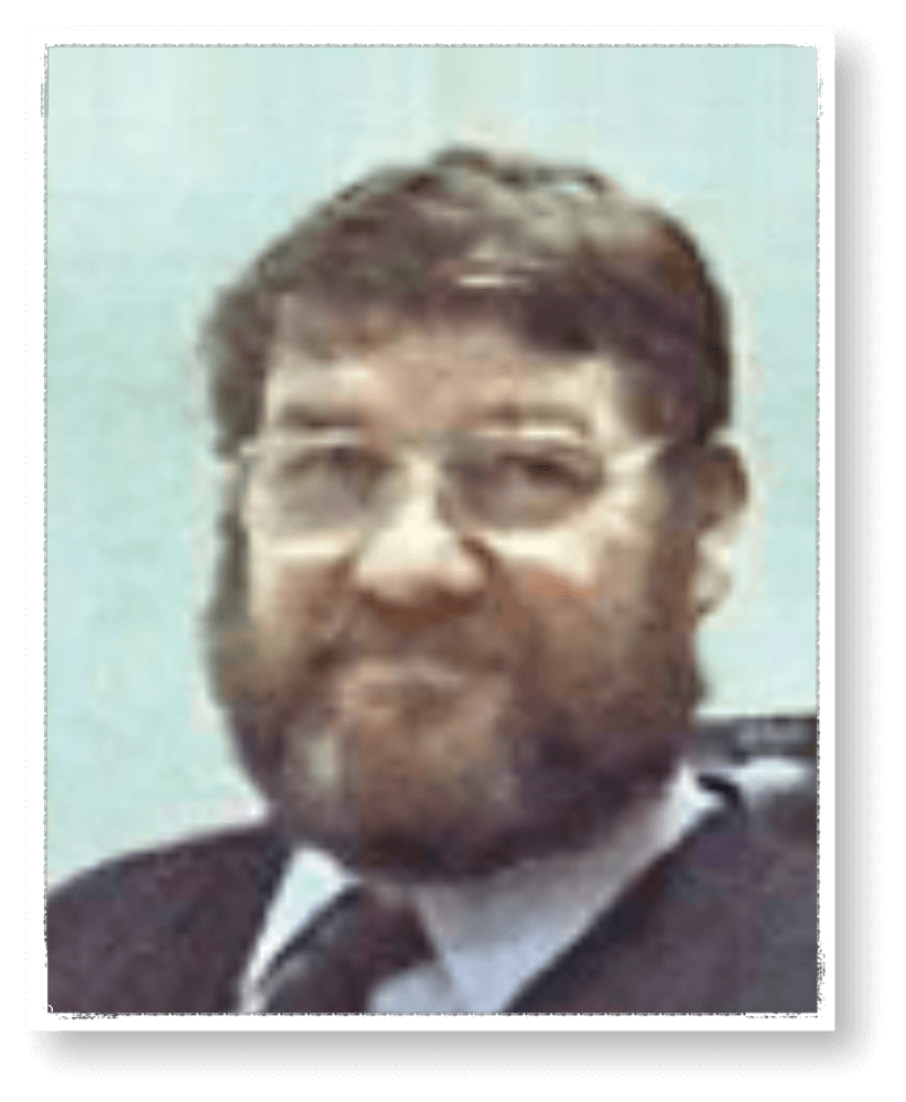 Porträt von Manfred Hasert, Sohn von Firmengründer Edwin Hasert und Vater von Jens Hasert; das unscharfe Farbfoto zeigt ihn mit Brille, Vollbart und Anzug vor hellem Hintergrund.